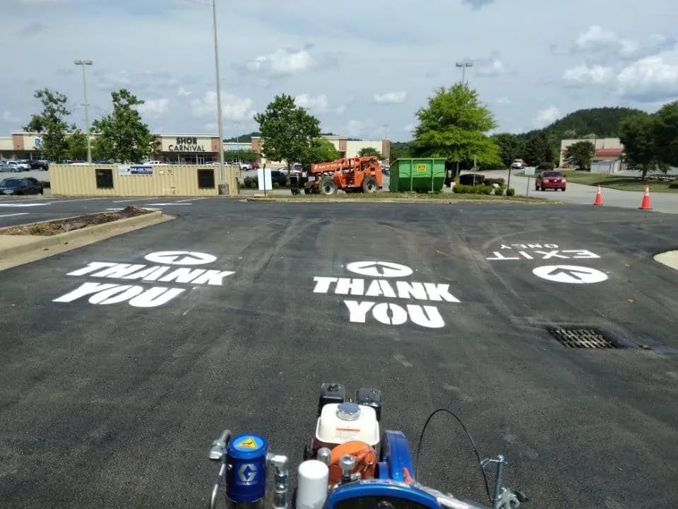 A parking lot striping machine sits on fresh asphalt marked with white 