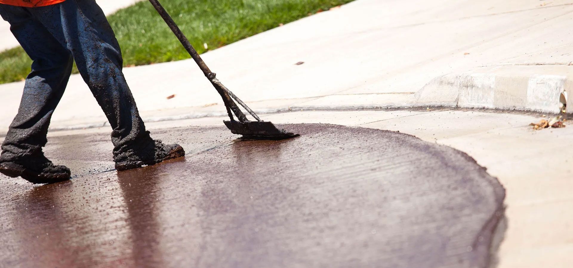 A person uses a squeegee to spread black asphalt sealant across a residential driveway.