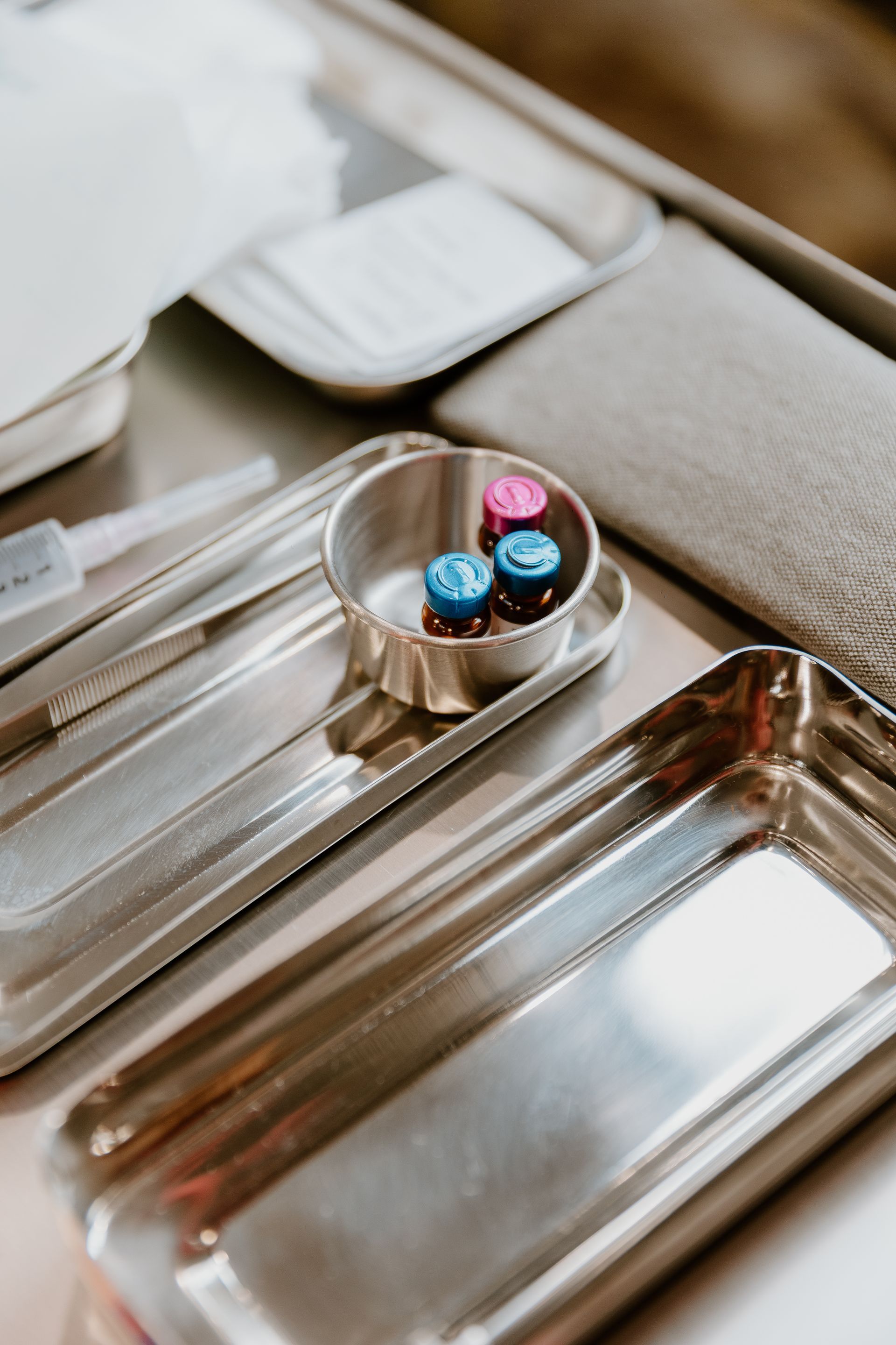 A metal tray holding dental tools, a small dish with two blue and one pink vial, and sterile gauze on a clinical table.