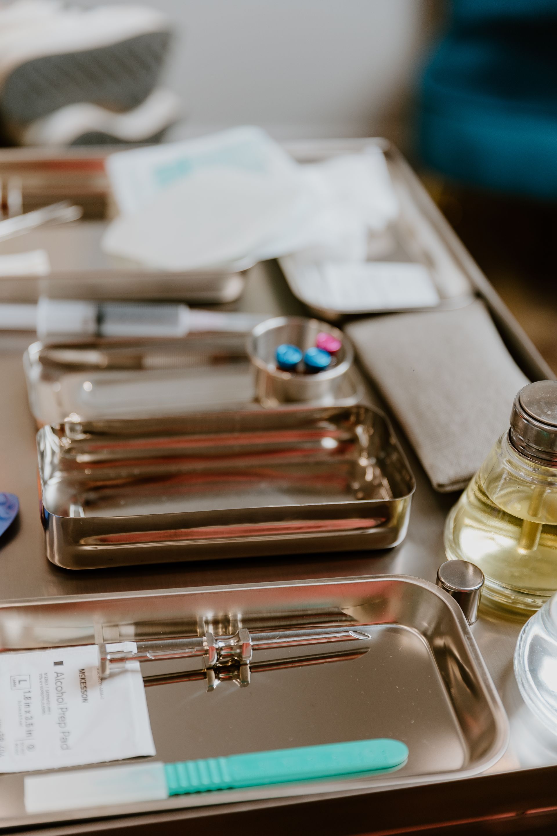 A medical tray with metallic tools, gauze, small vials, and a turquoise handled instrument on a clinical surface.
