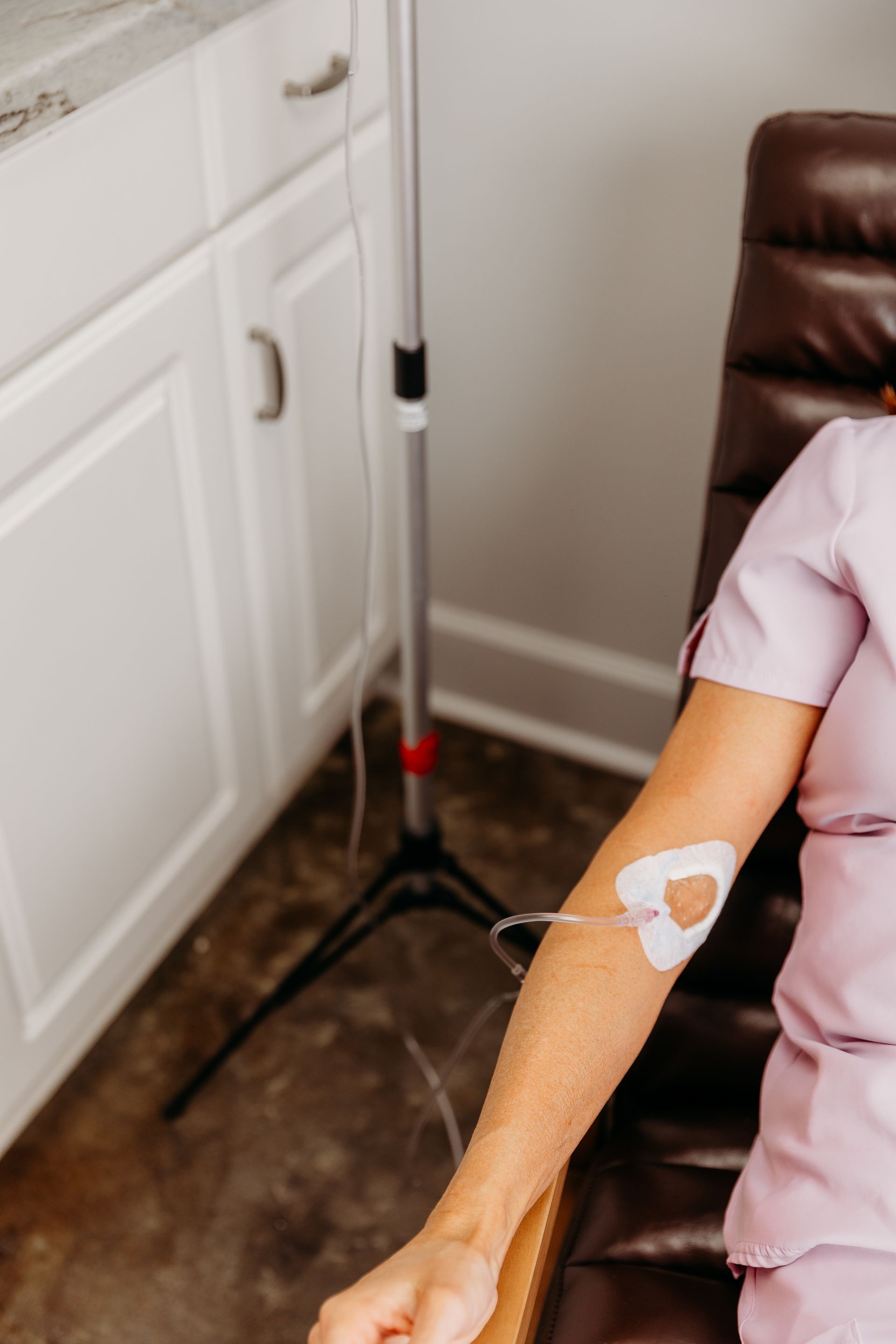 A person sits in a chair receiving intravenous therapy with a tube connected to a patch on their forearm.