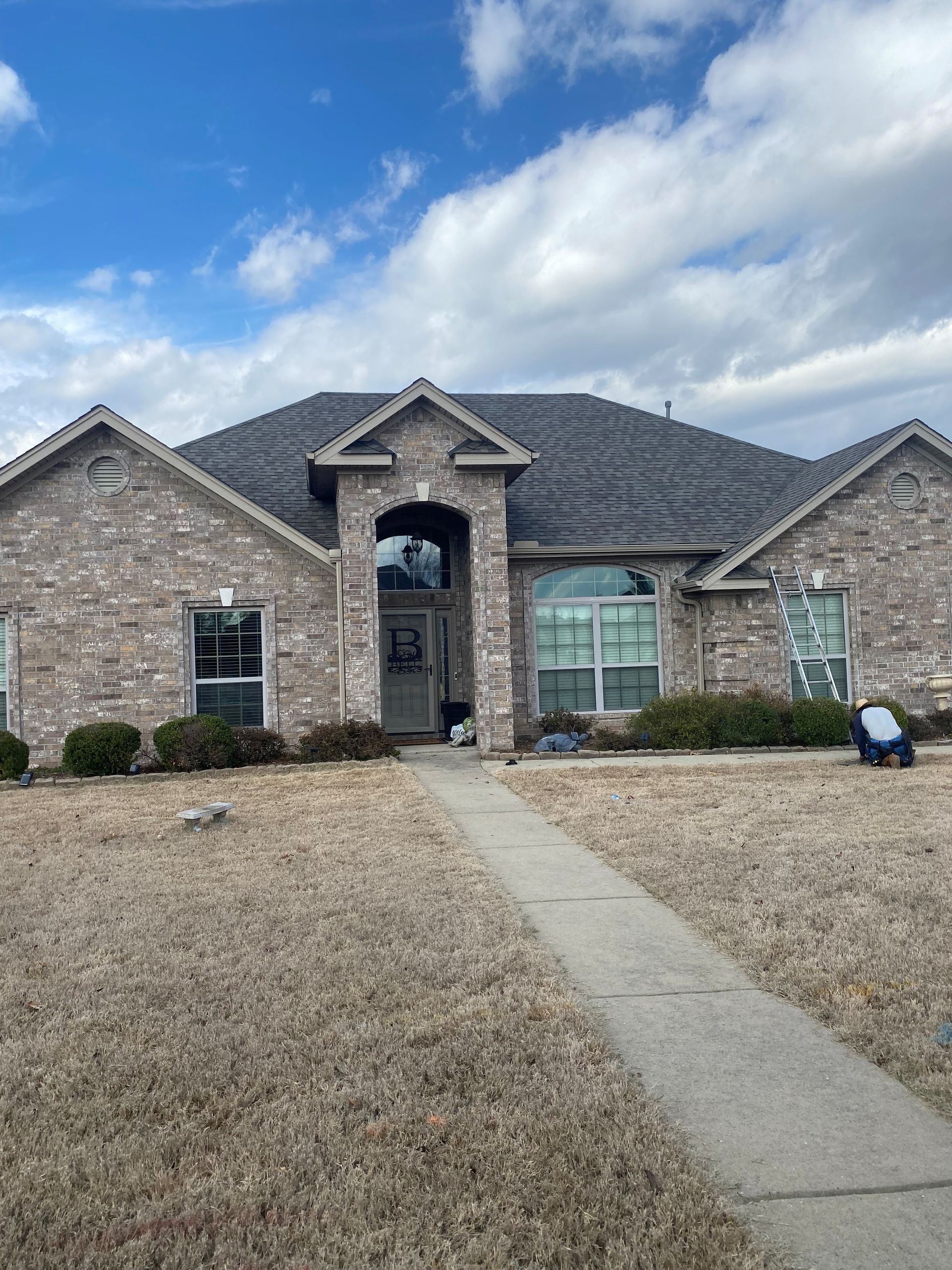 Brick house with dark roof and blue sky. Sidewalk leads to the front door. Man on right side.
