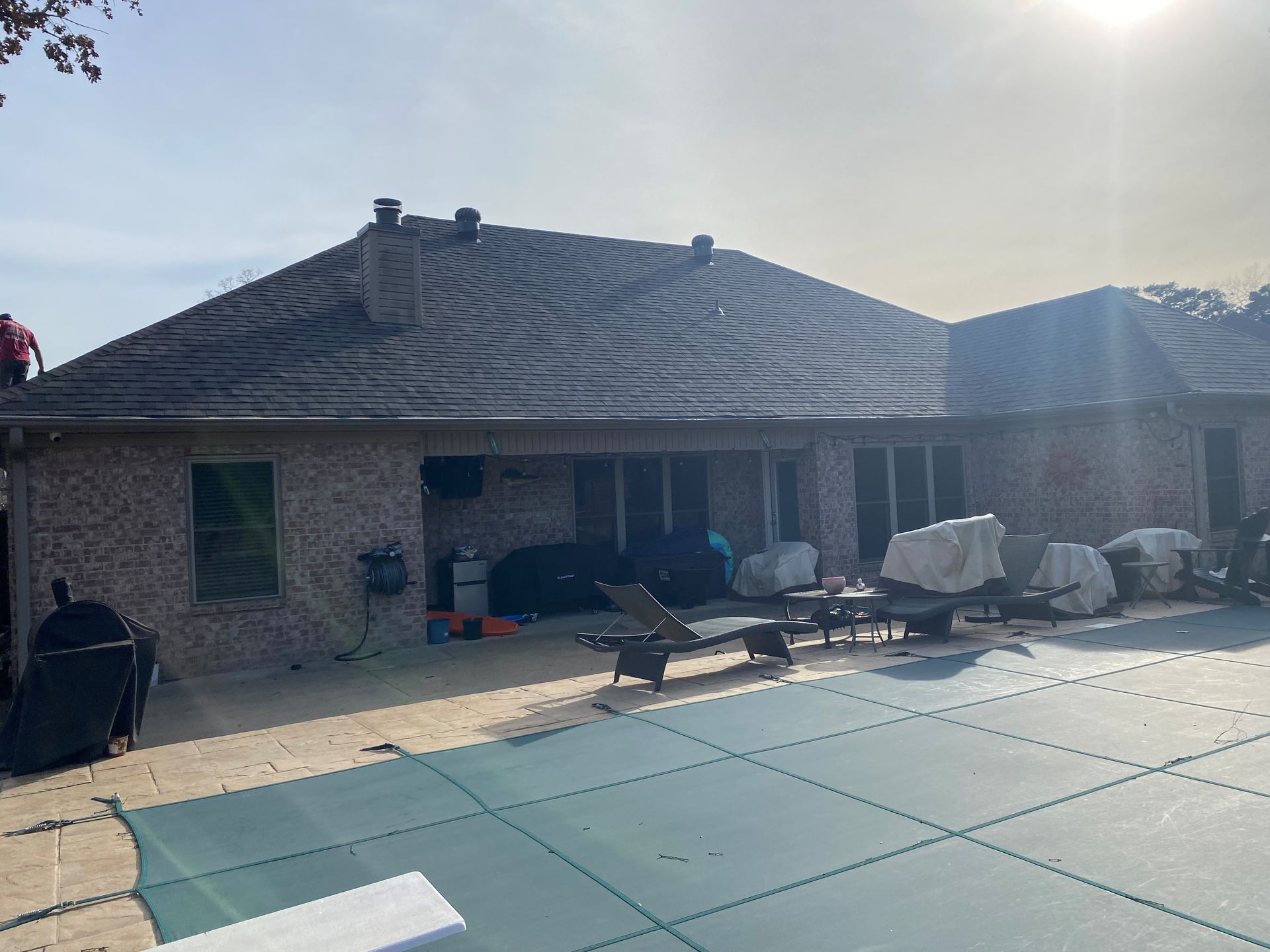 Backyard with pool, patio, and brick house under sunny sky.