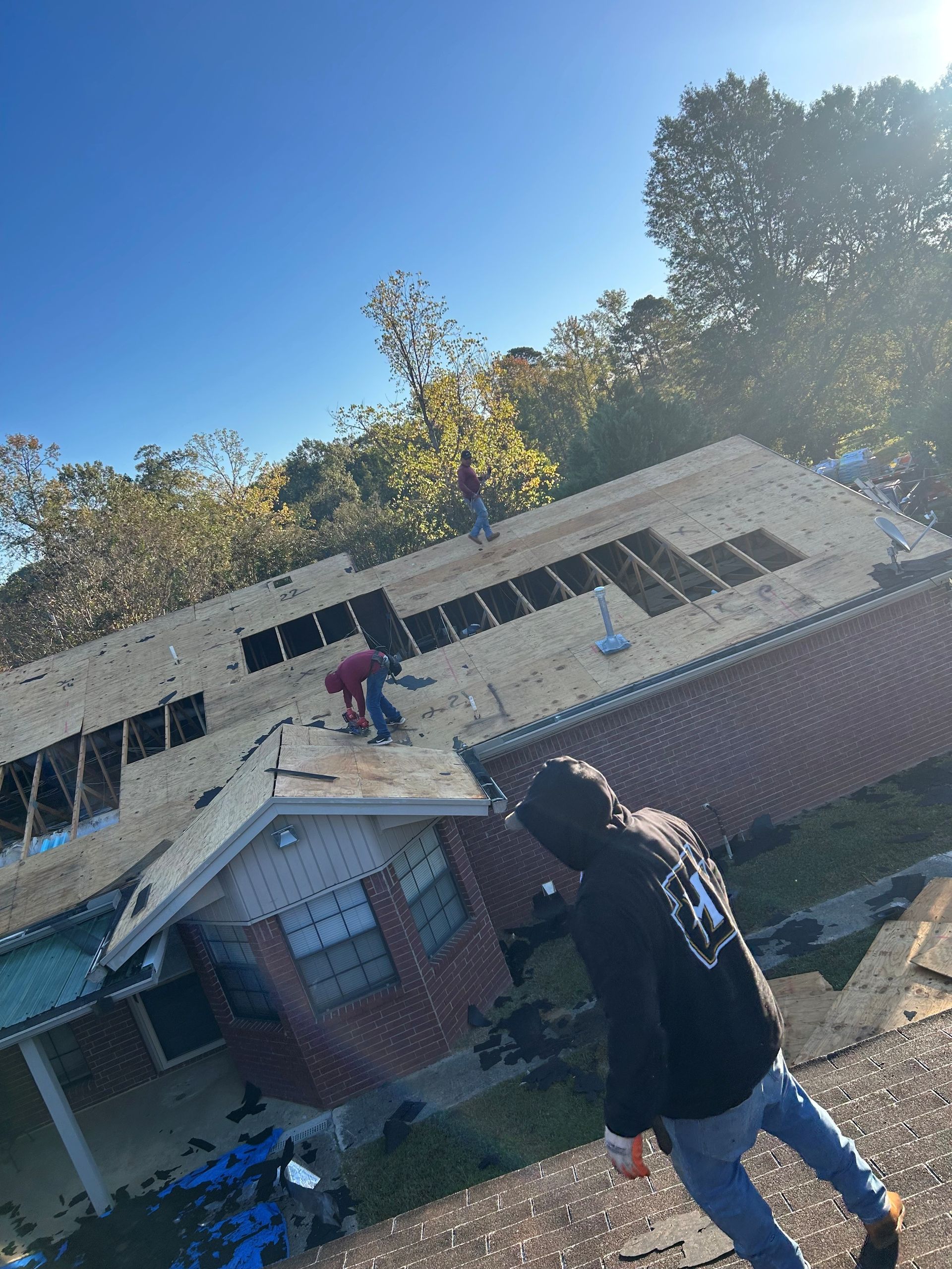Roofers working on a house roof. Blue sky, trees in background.