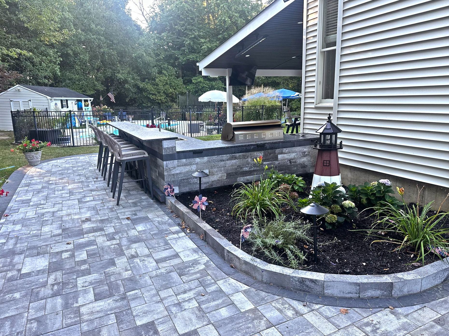 Patio with a built-in bar, surrounded by a garden and a house with a gray siding.
