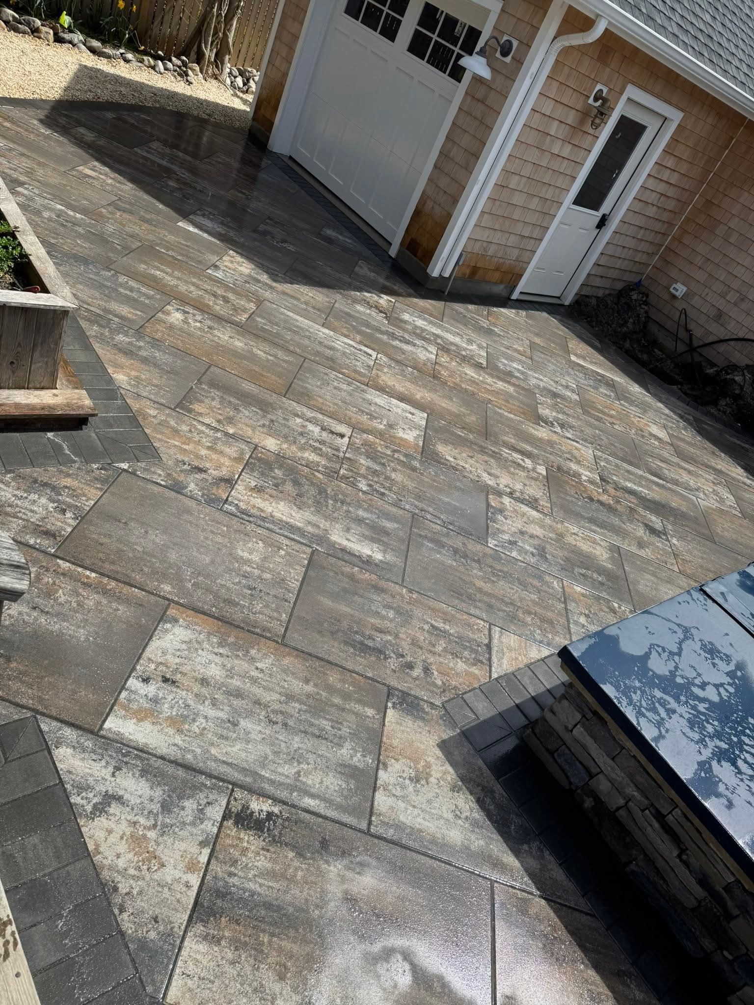 Patio with textured pavers leading to a garage, with a small side door and dark edging, natural light.