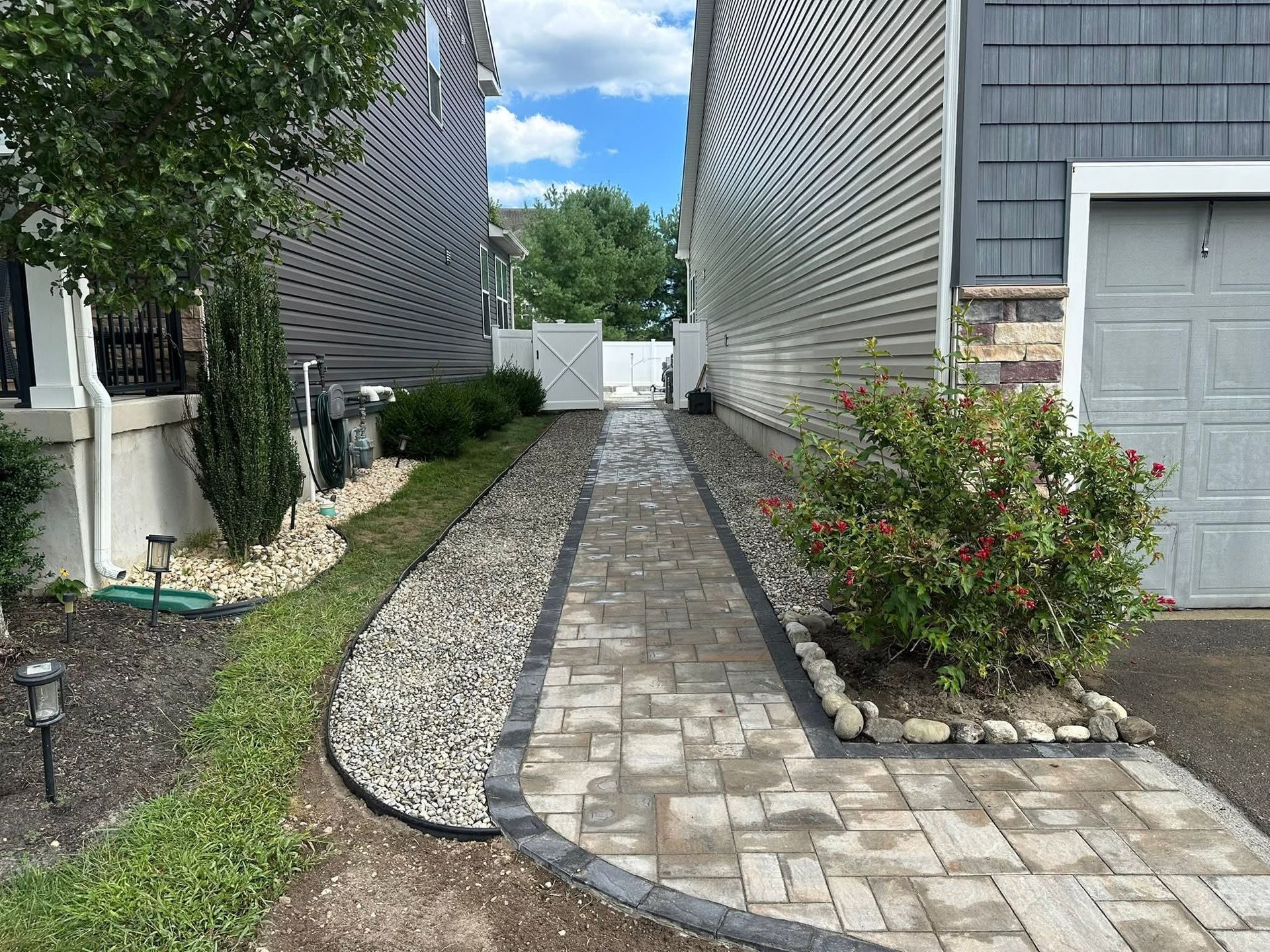 Brick pathway between houses, bordered by gravel and landscaping.
