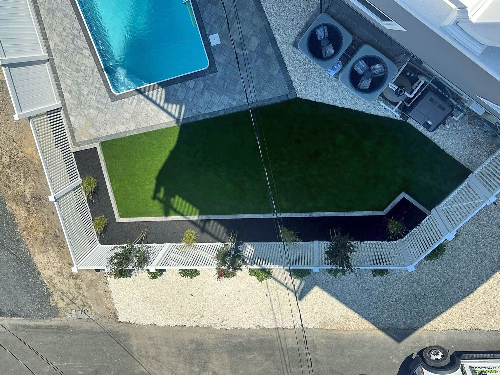 Overhead view of a backyard with pool, grass, fence, and AC units.