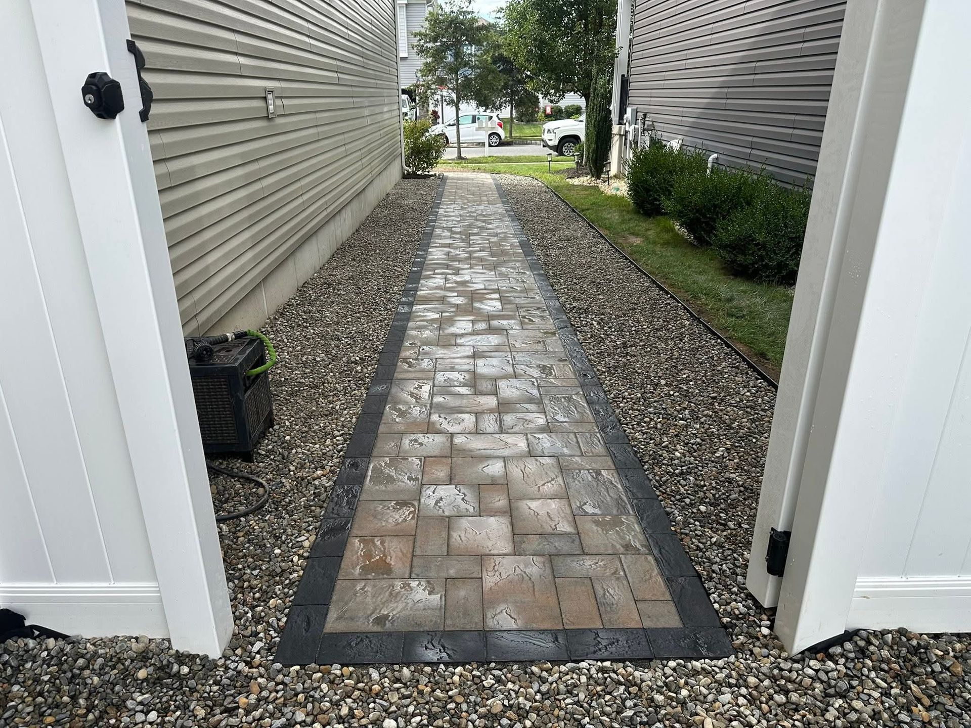 Brick pathway between buildings, gravel edges, and opening white gate.