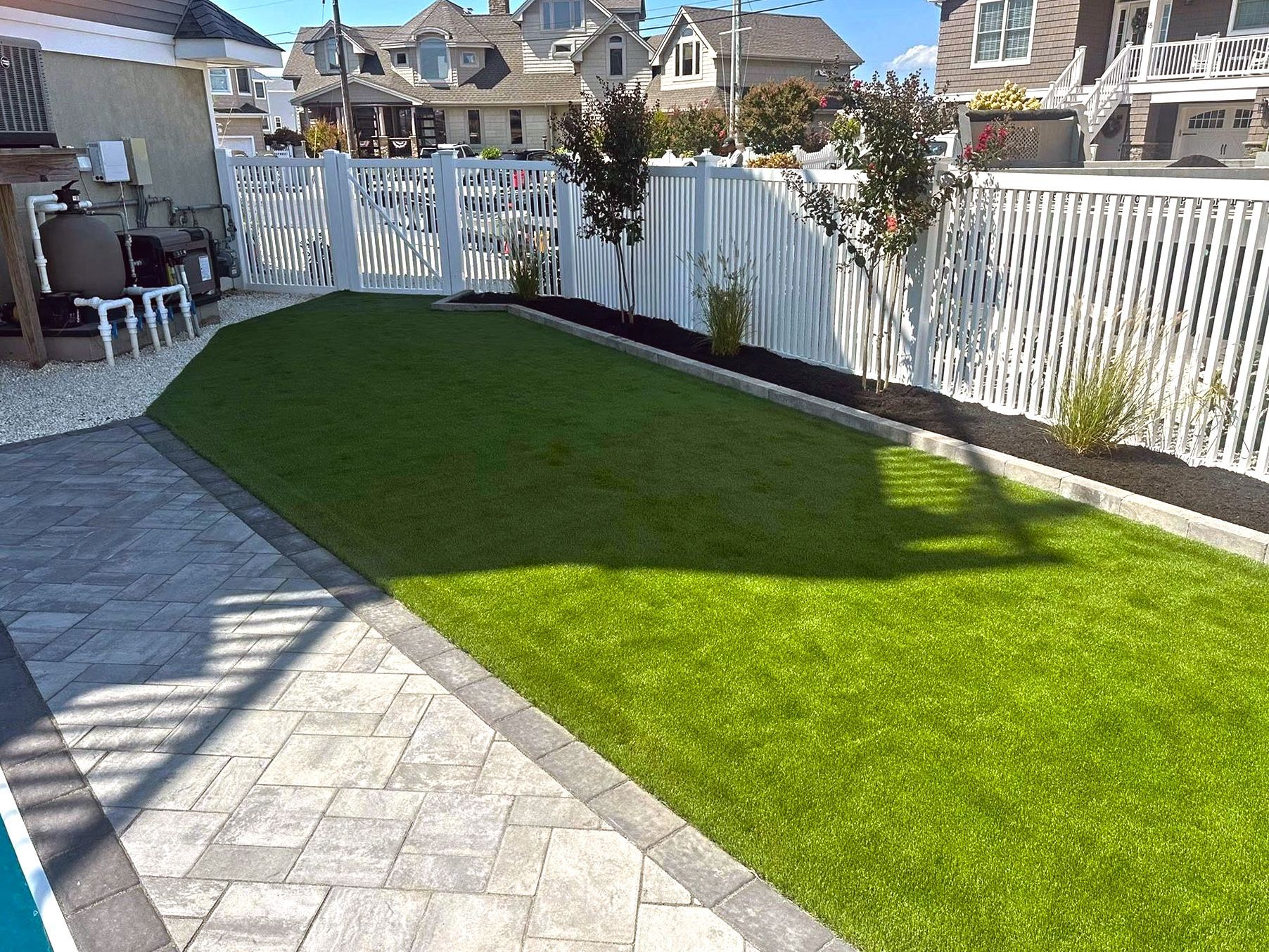 A manicured backyard with a green lawn, white fence, and a brick pathway.