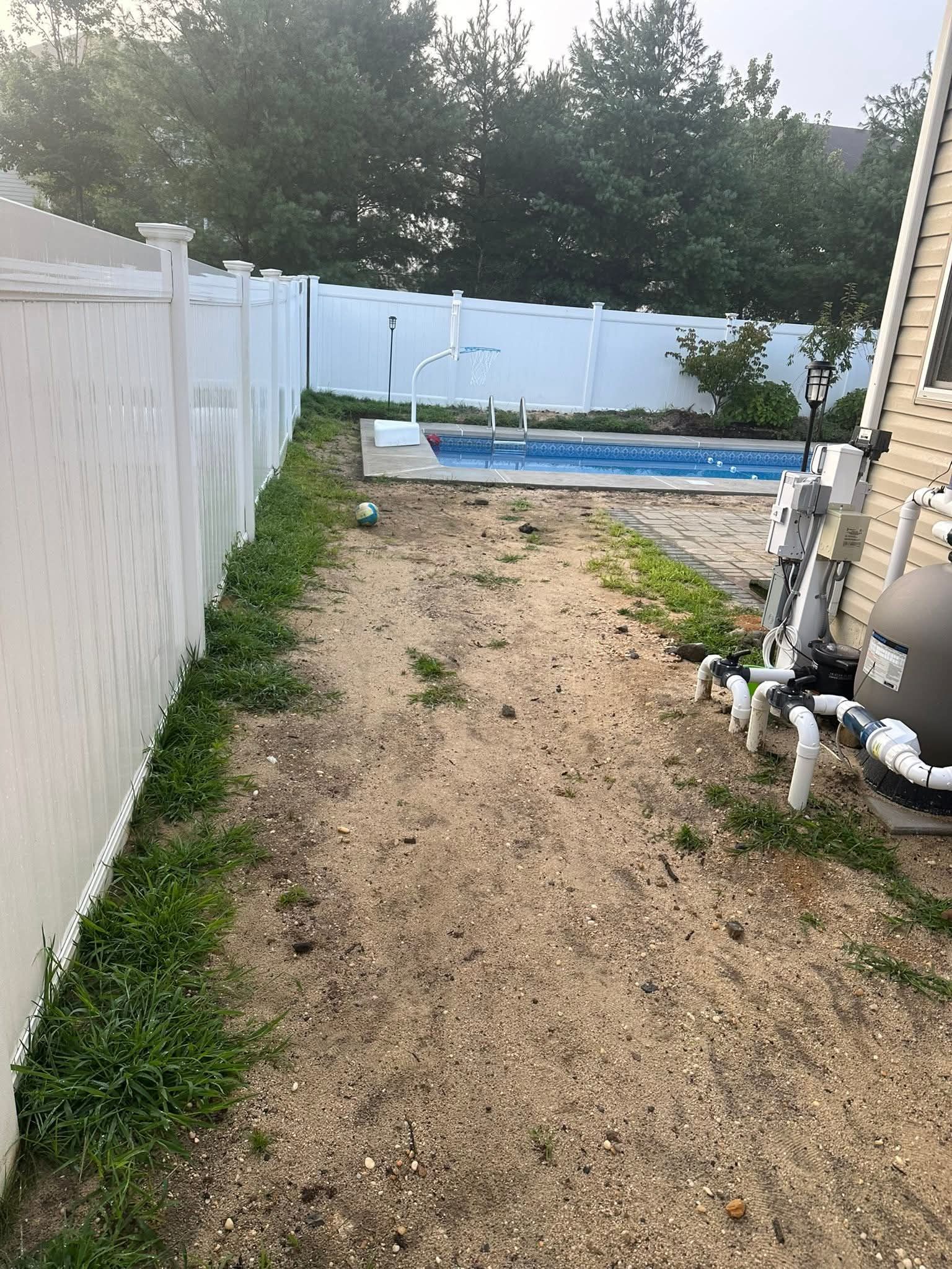 Backyard with a small pool, sand and dirt path, white fence and equipment.