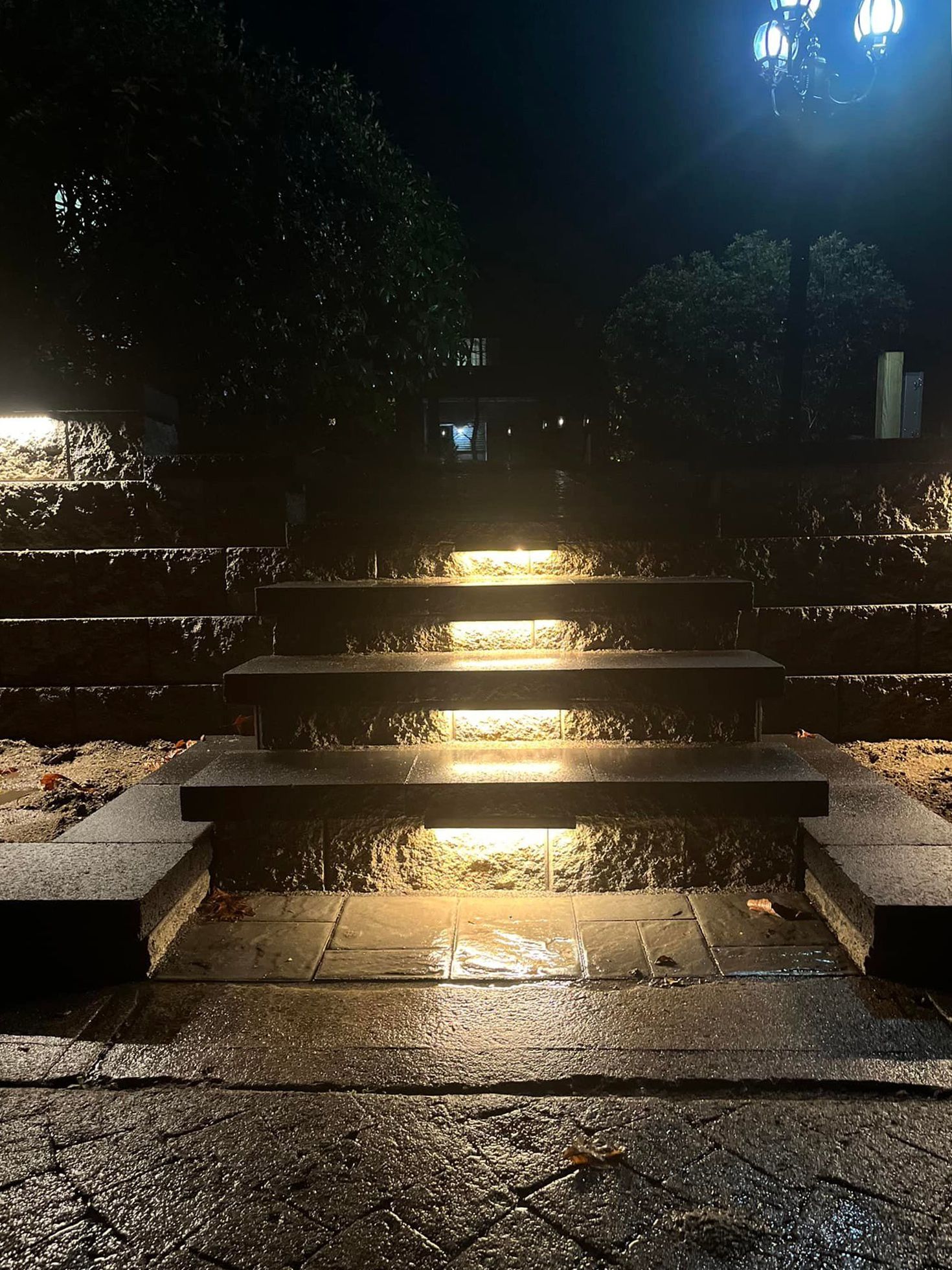 Wet stone steps illuminated at night, leading upwards.