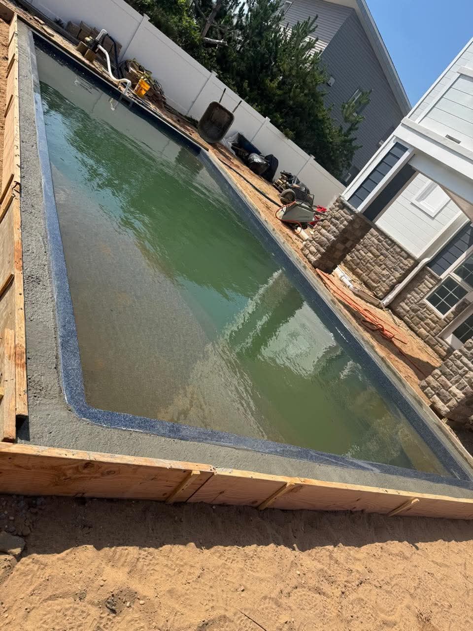 Pool construction: partially built rectangular pool with green water surrounded by wooden framing and a home.