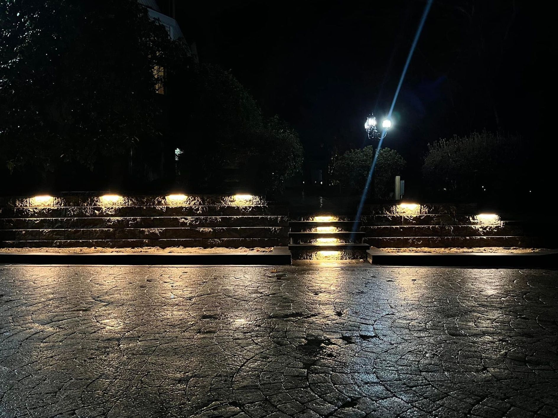 Rain-slicked steps illuminated at night, with glowing lights and a streetlight in the distance.