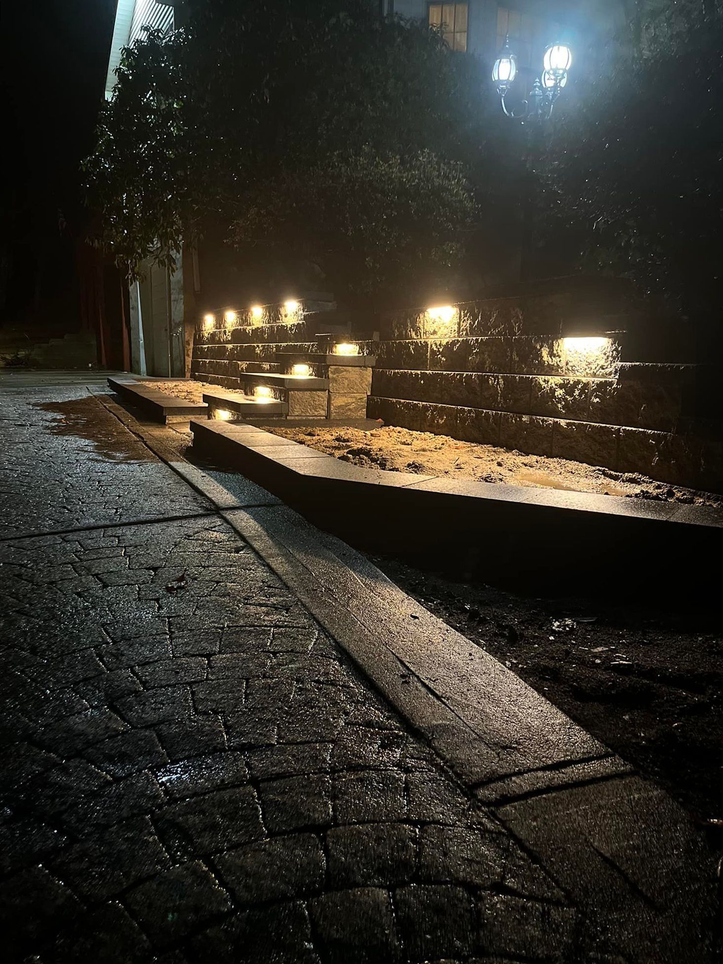 Wet cobblestone path at night with lit steps, building in background.