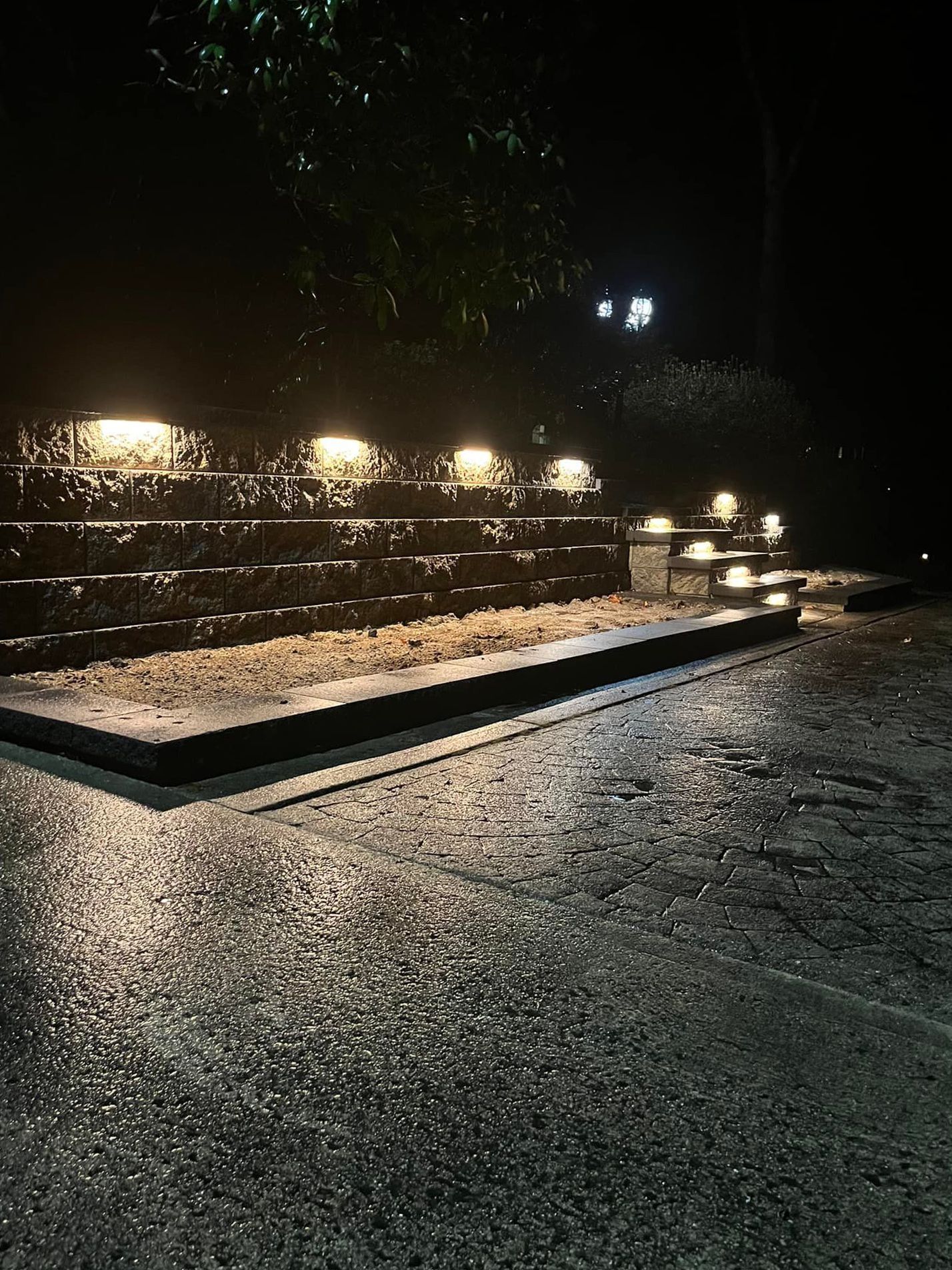 Night shot of illuminated stone steps; wet pavement reflects light.