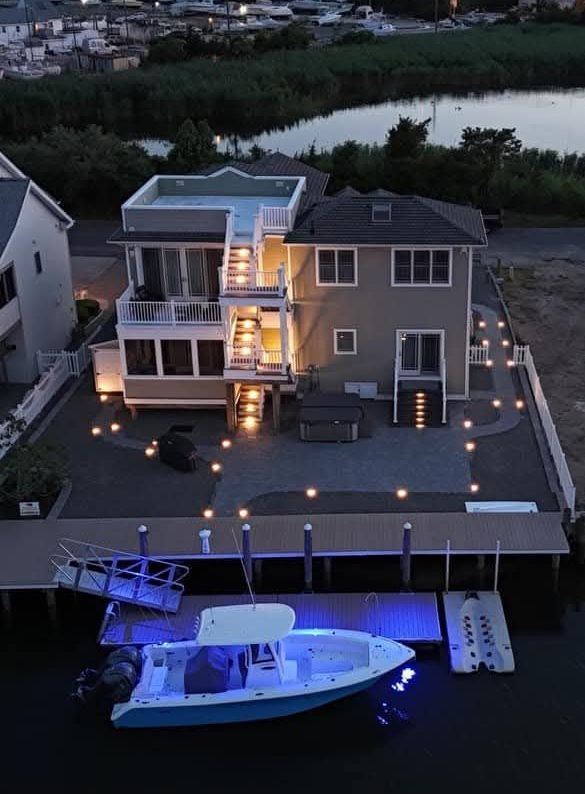 House on a canal at dusk; boat docked with blue lights, string lights, steps to upper levels.