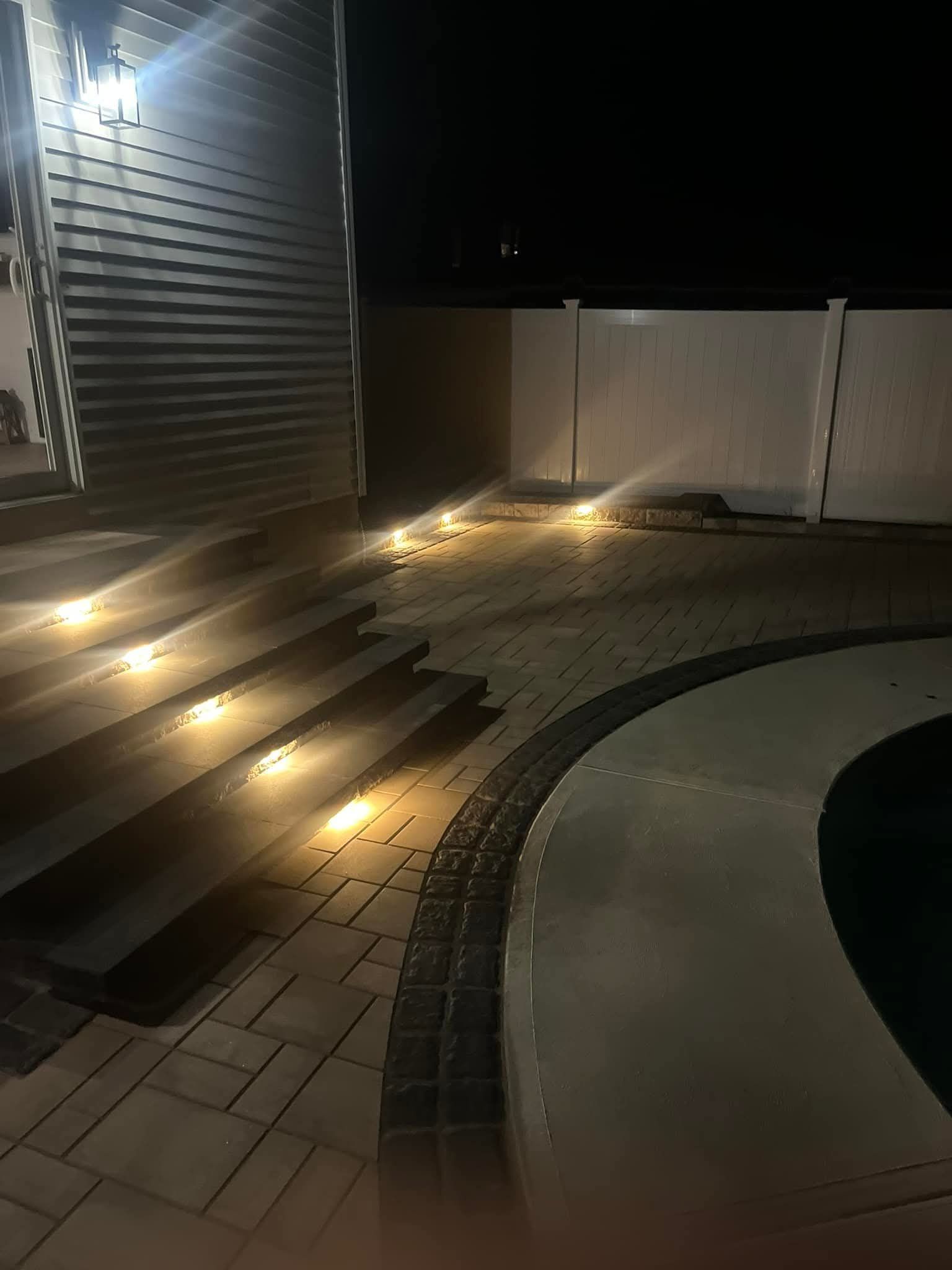 Exterior night shot of illuminated steps, pavers, and pool area.