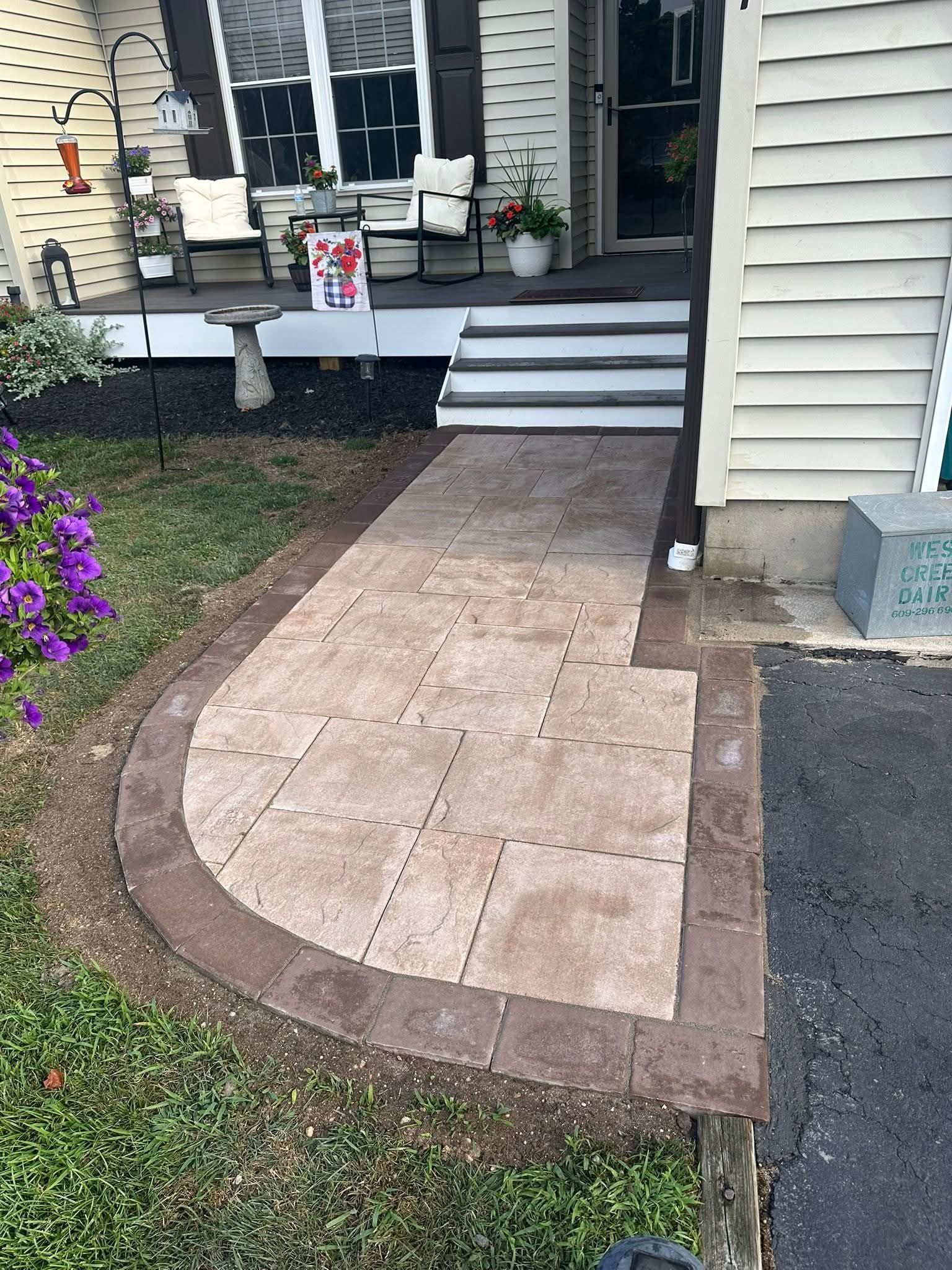 Paver walkway leads to porch with steps. Brown pavers, dark brown border.
