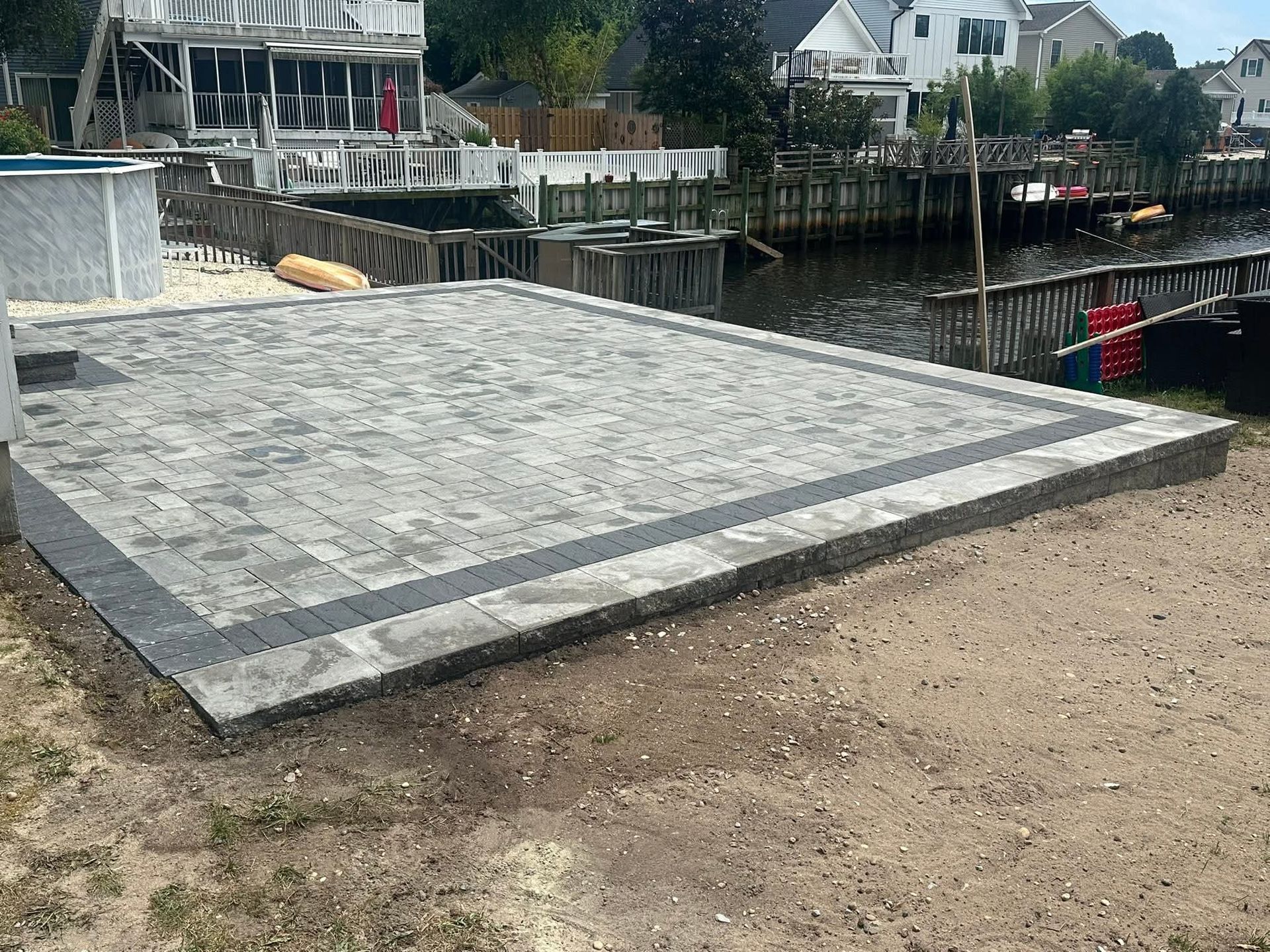 Gray brick patio overlooking a waterway with houses, docks, and a sandy area.