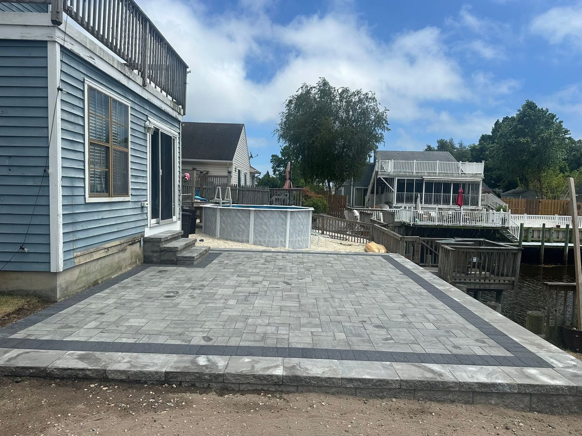 Blue house with patio, pool, and waterfront view on a sunny day.