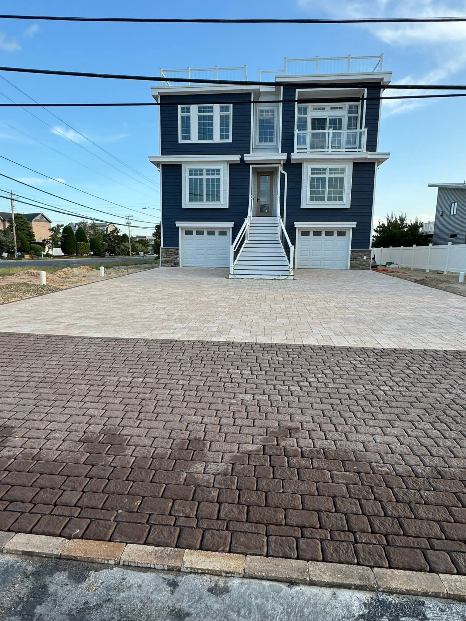 Three-story blue house with white trim and three garage doors. Paver driveway.