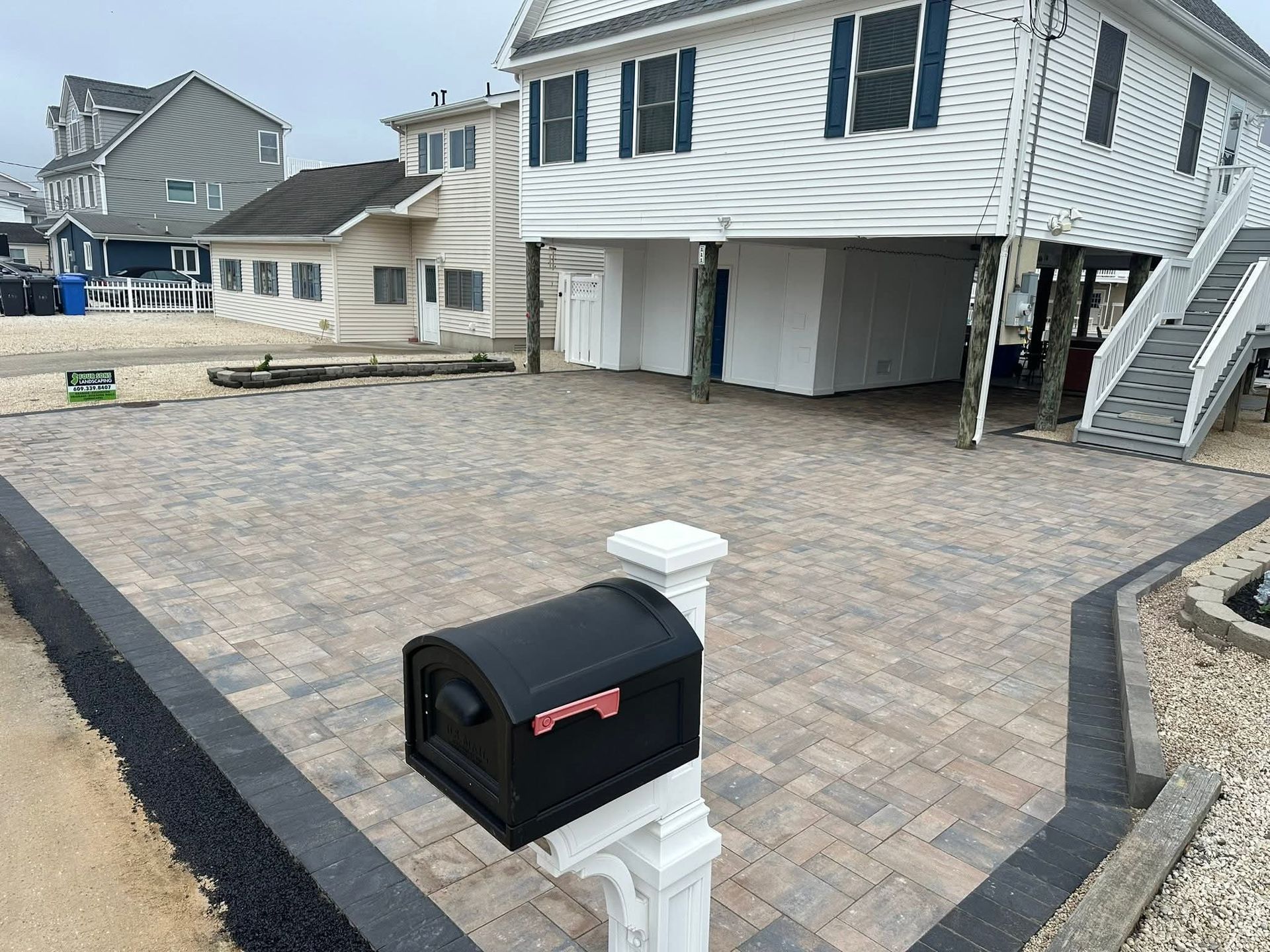 Paver driveway and a mailbox in front of a raised white beach house.
