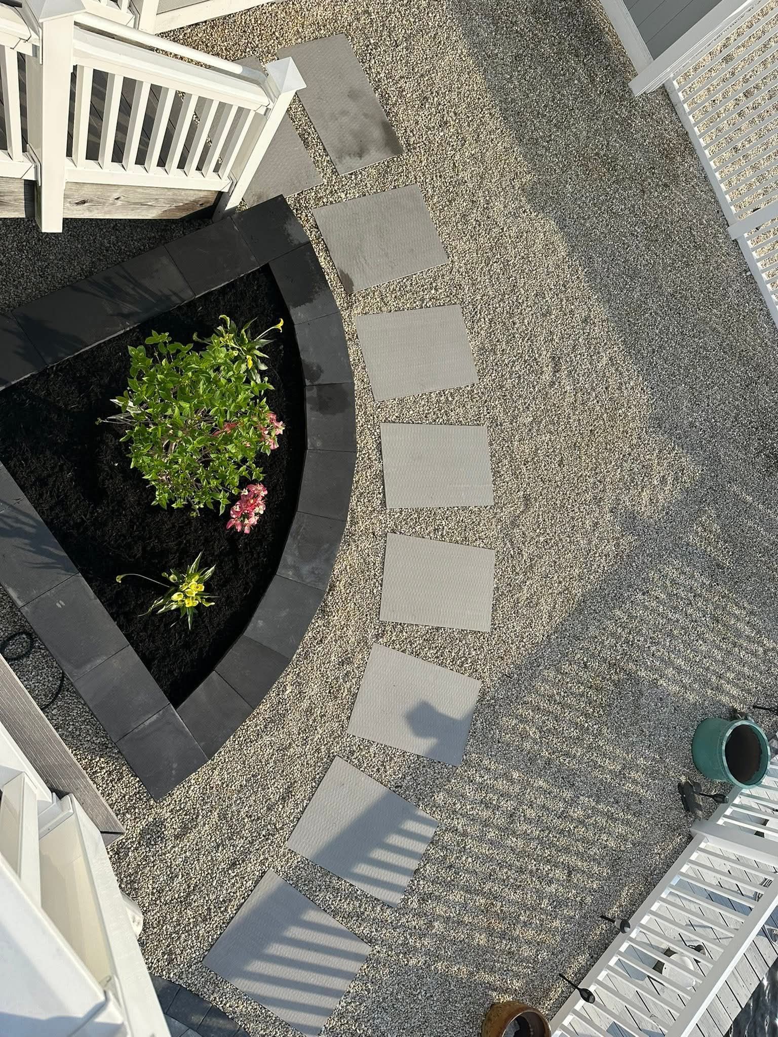 Overhead view of a garden with stepping stones leading from a black-edged flower bed on gravel.