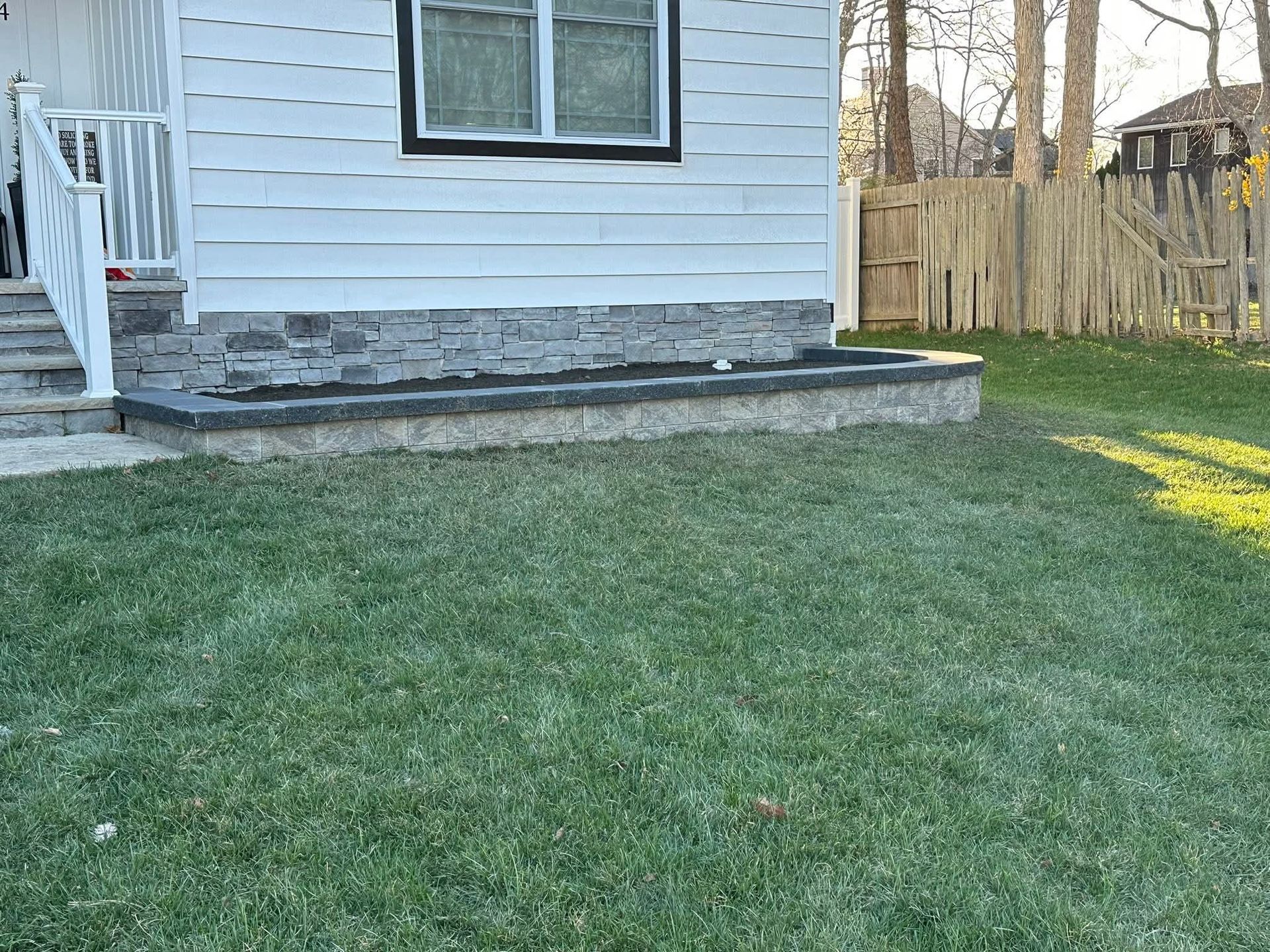 A white house with a stone base and green lawn. A window is visible.