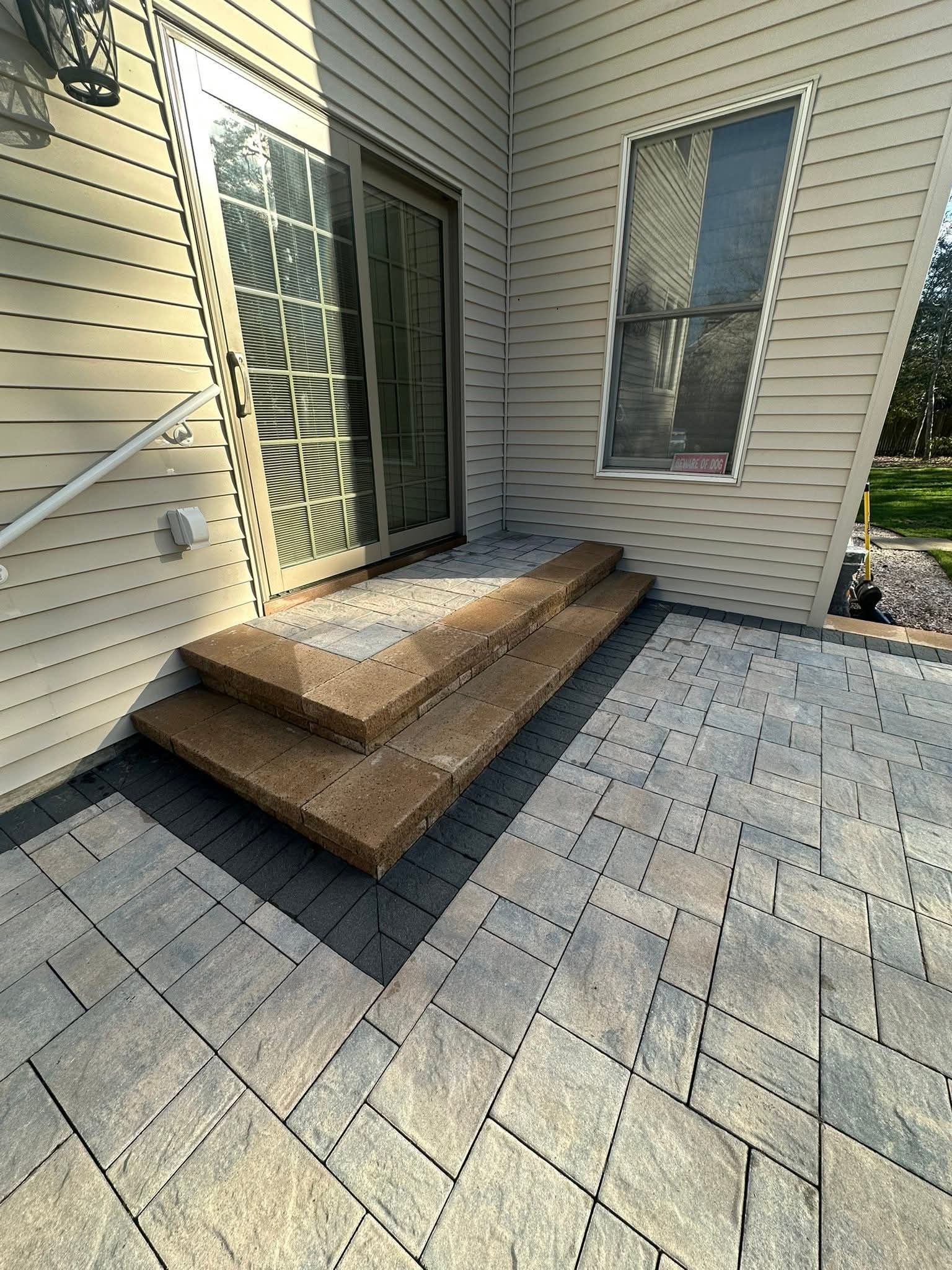 Steps leading to a sliding glass door on a house with a paved patio.