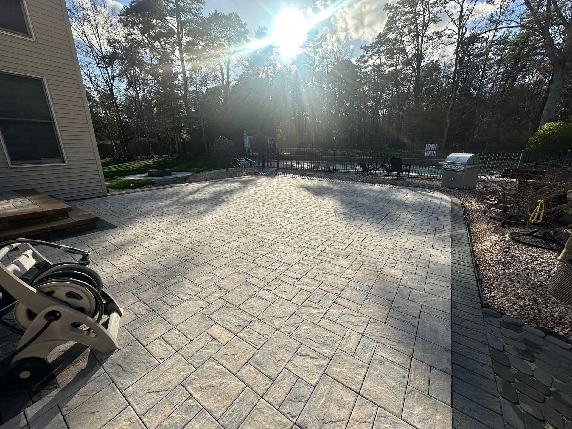 Sunlit outdoor patio with gray pavers, trees, and a house.