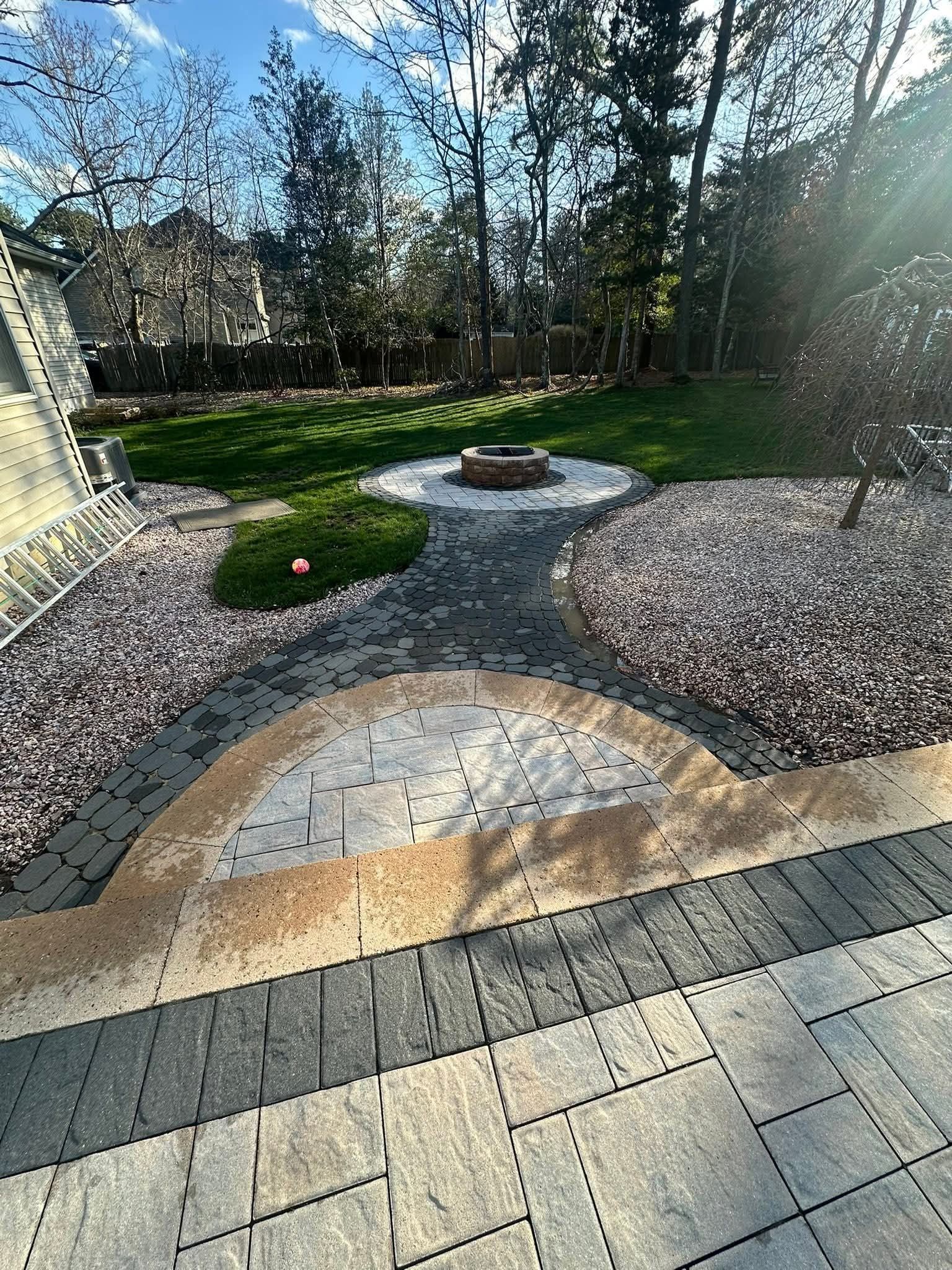 Backyard with a fire pit, pathway, landscaping, and green lawn.