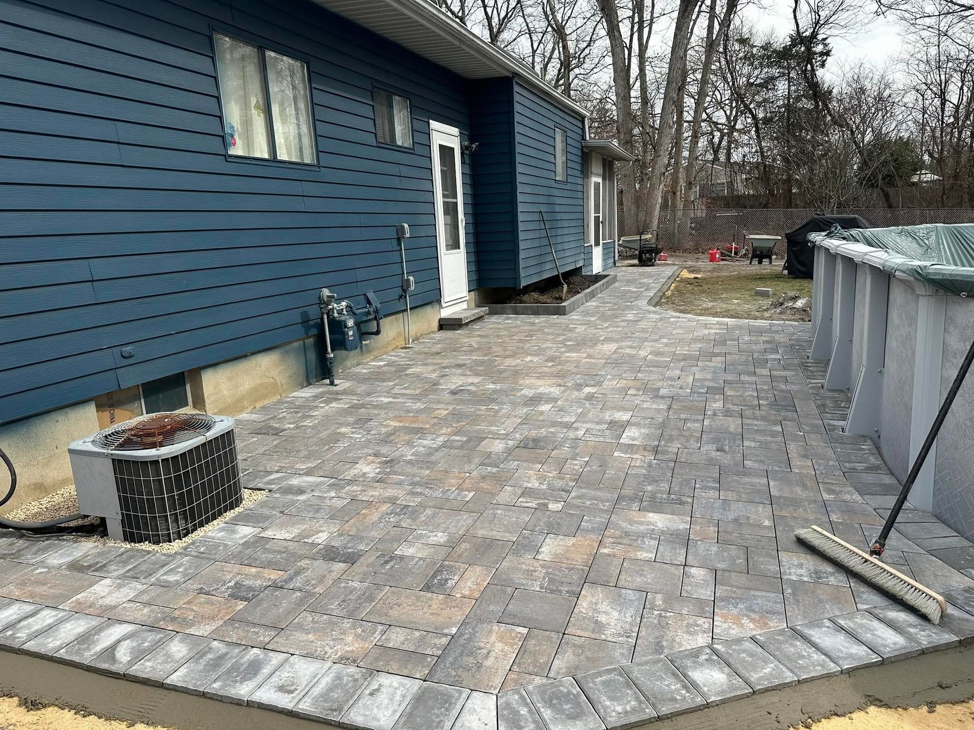 Blue house with a brick patio next to an above-ground pool.