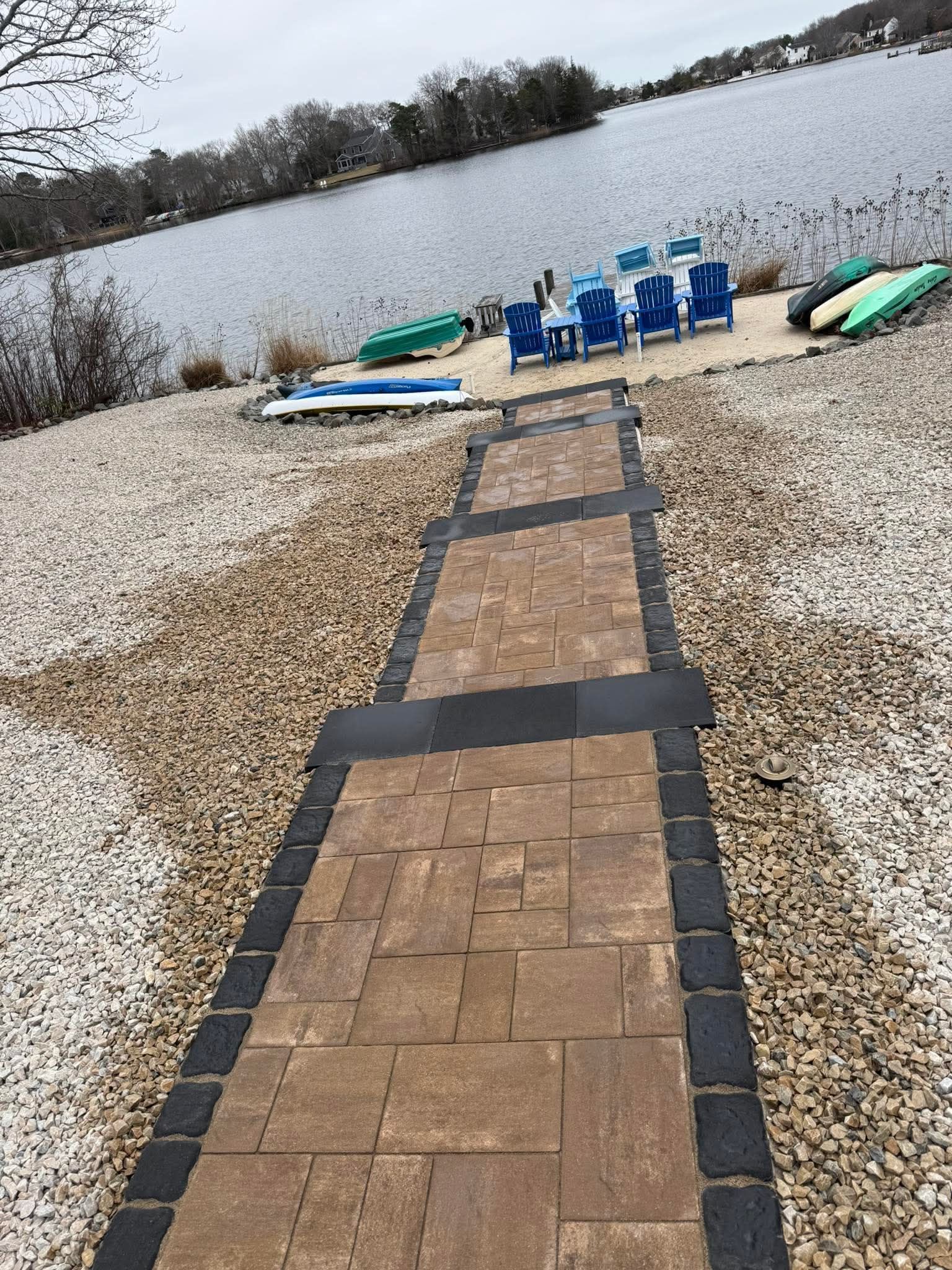 Brick pathway leading to lakefront with blue chairs and boats.
