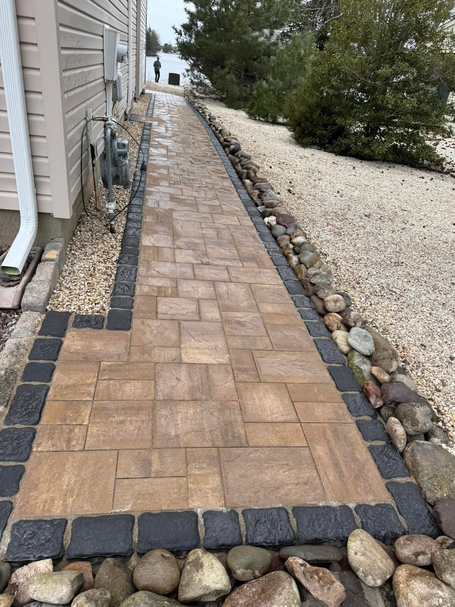 Brick pathway with stone edging, along a building and gravel area.