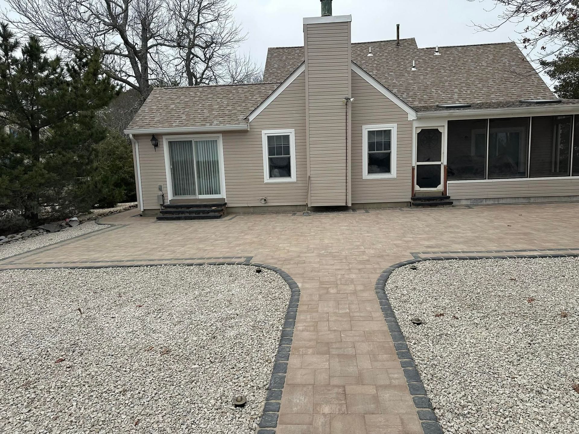 Tan house with gravel yard, brick pathway, and a screened-in porch.