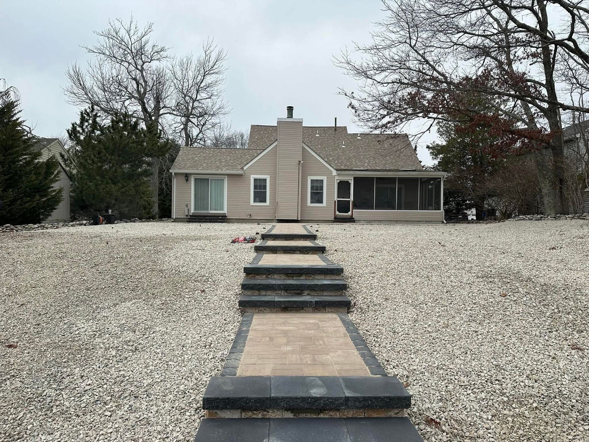 A tan-colored house with a brick and stone pathway leading to the front door on a gravel yard.