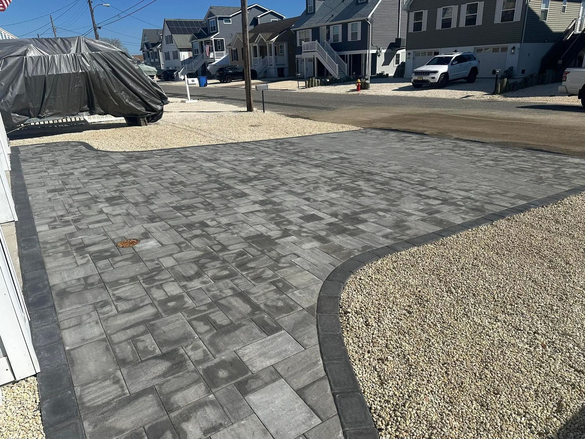 Driveway paved with gray blocks, surrounded by tan gravel, with houses in the background.