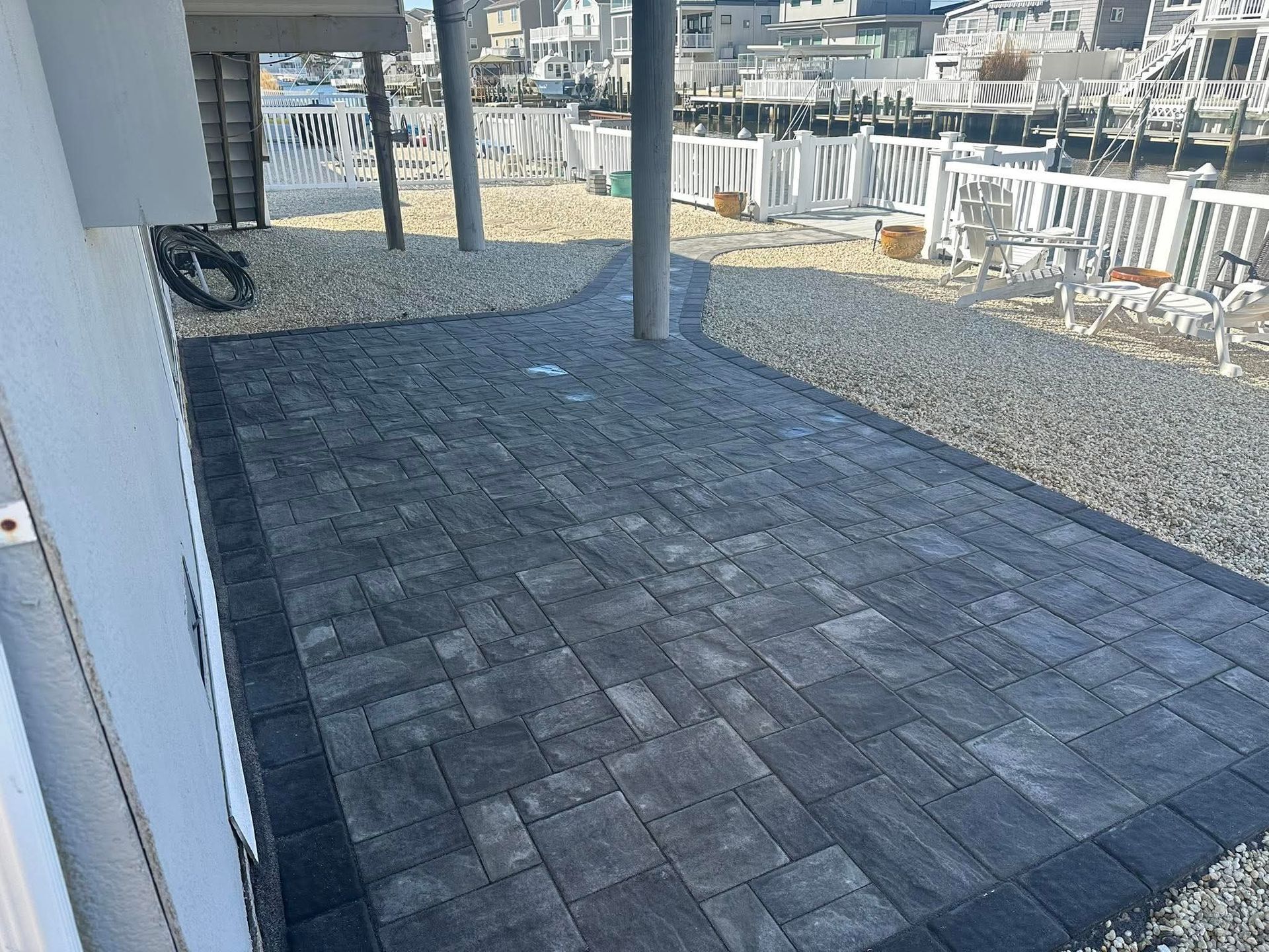 Paver patio with gray gravel, under a white structure. Near a waterfront.