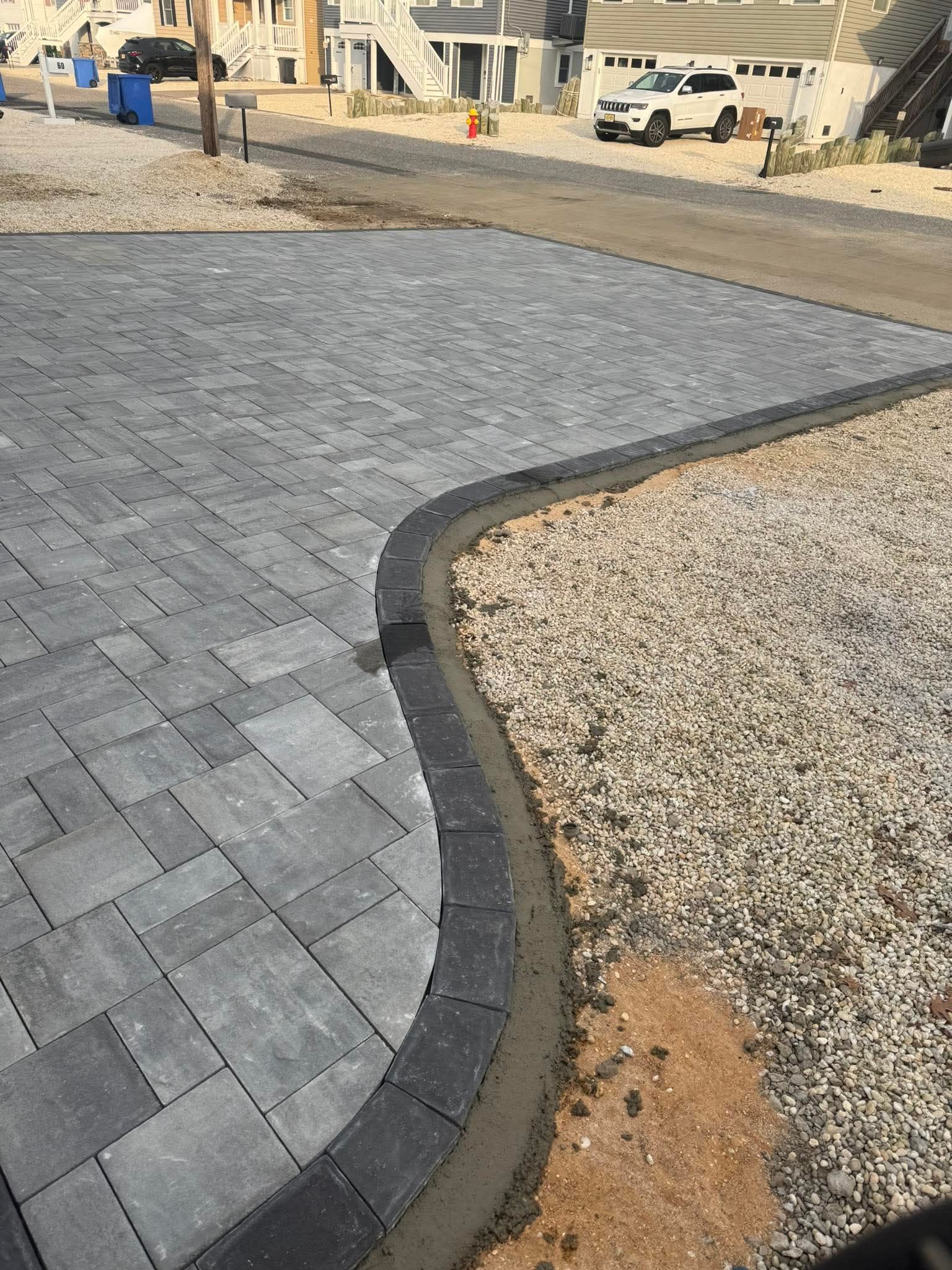 Brick pavers curving alongside a gravel driveway, with cement border; construction scene.