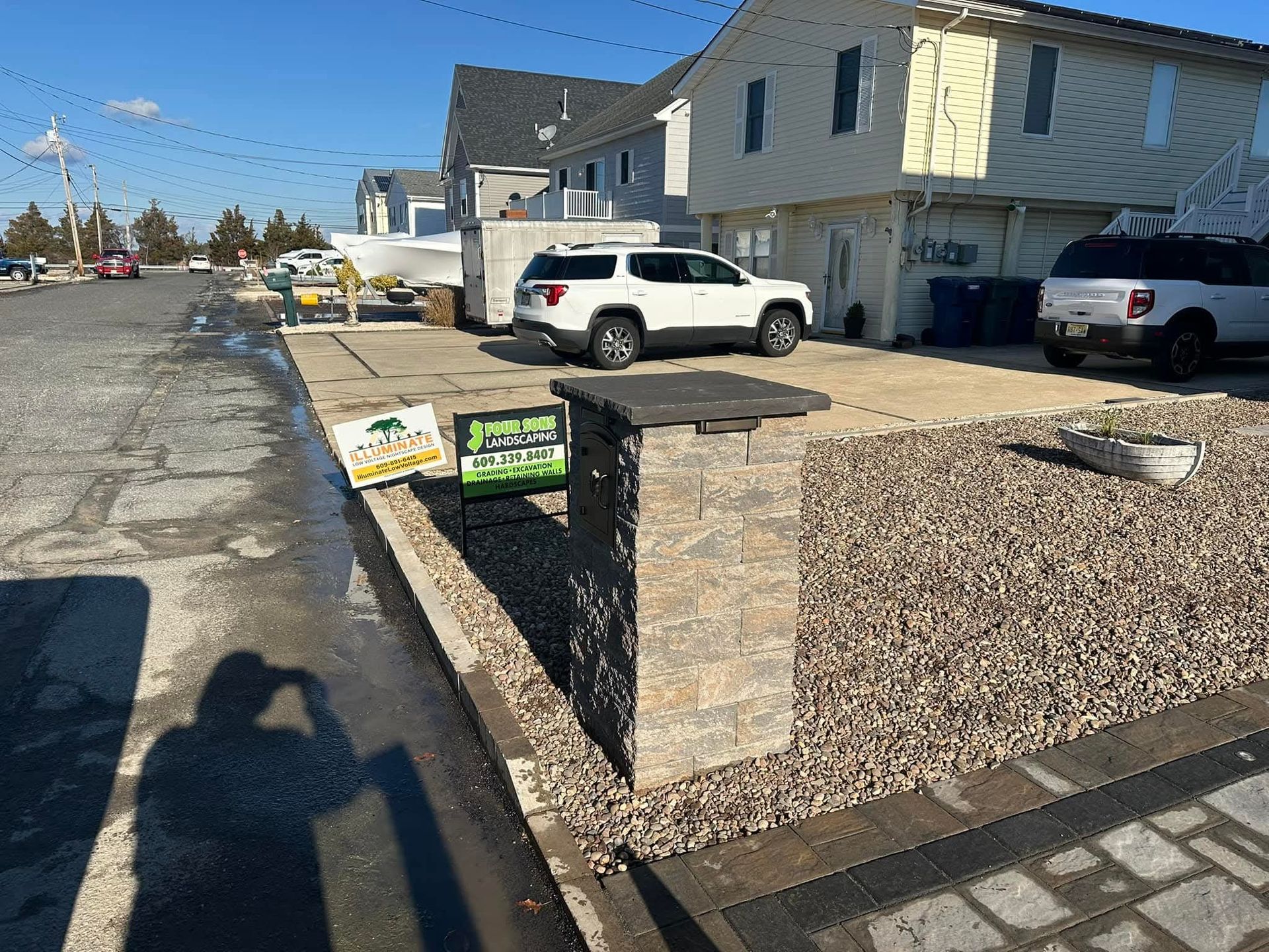 A stone pillar with two signs in front of a building with cars parked in a driveway.