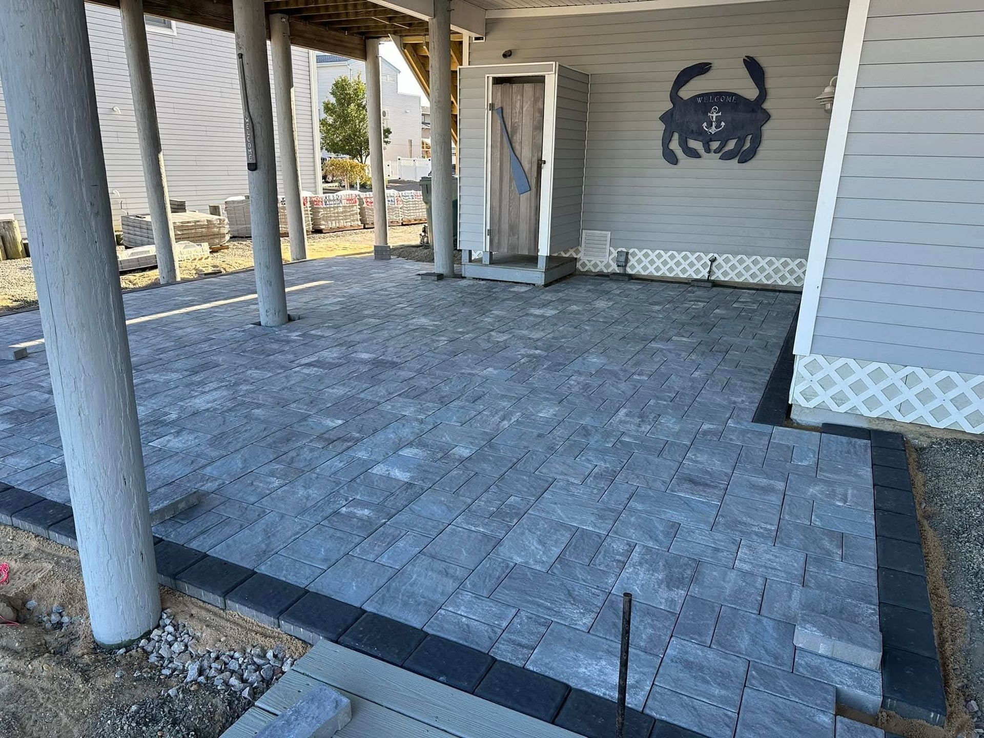Gray paver patio with a black border under a house with a crab wall art.