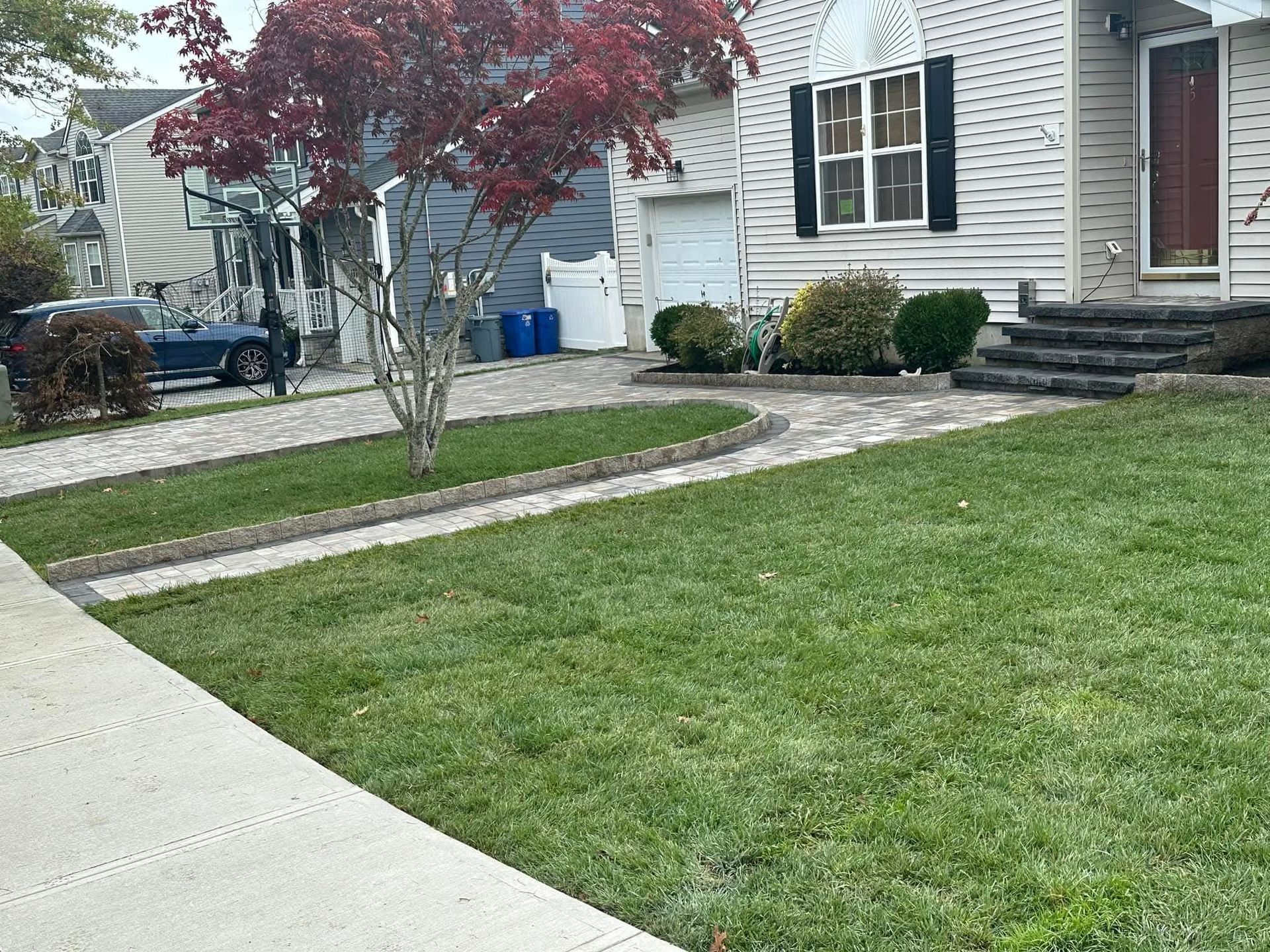 House exterior with brick driveway, green lawn, and red-leafed tree.