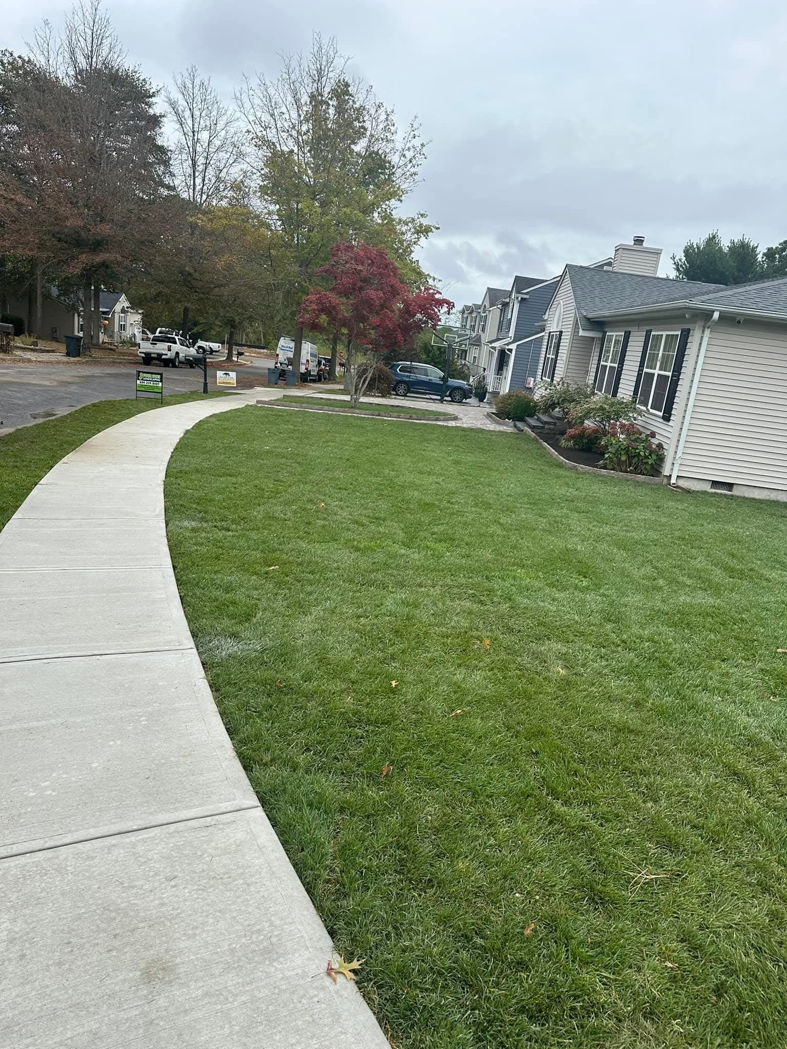 Sidewalk curves past green lawn and townhouses under cloudy sky.