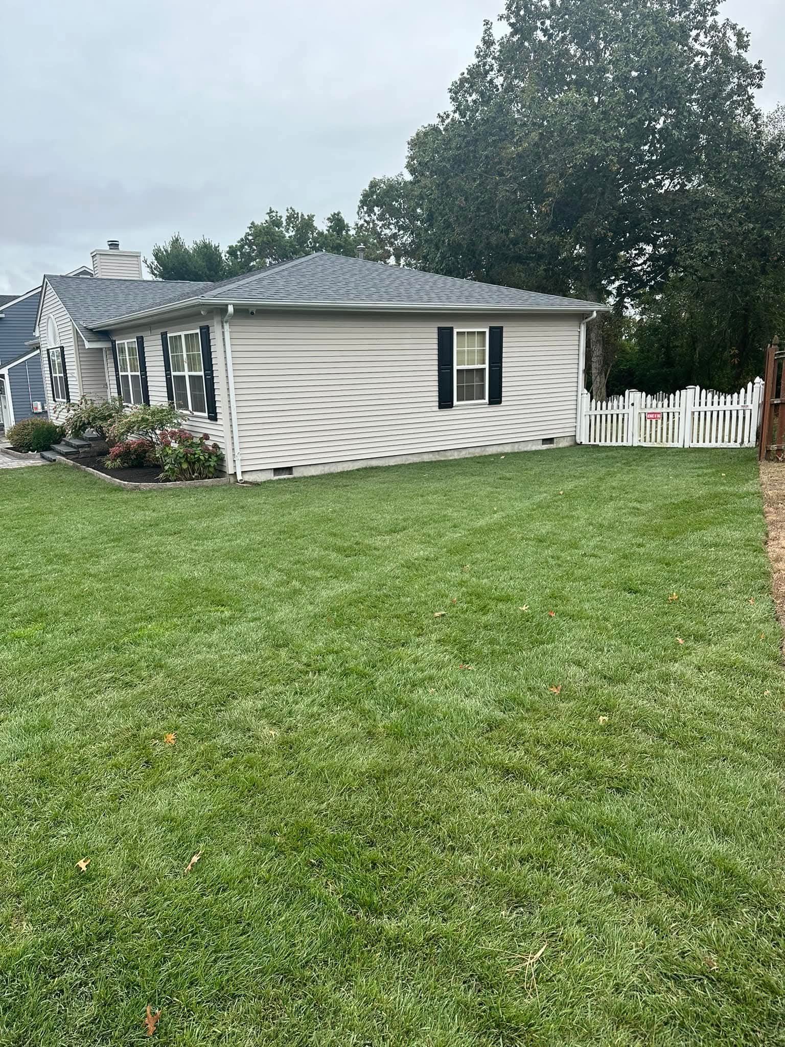 A house with gray siding and a white picket fence in front of a green lawn.