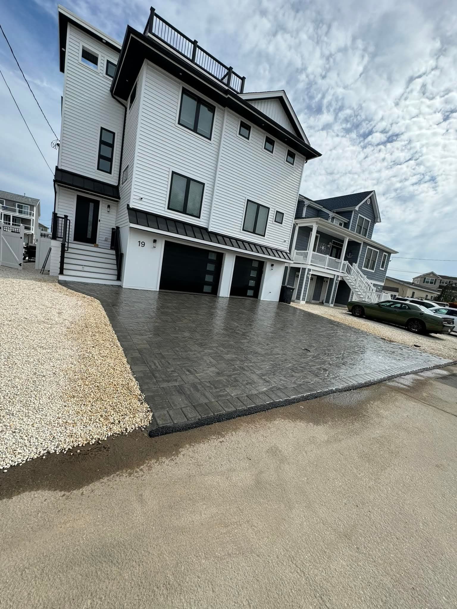 Modern white and black multi-story house with paved driveway and coastal setting.