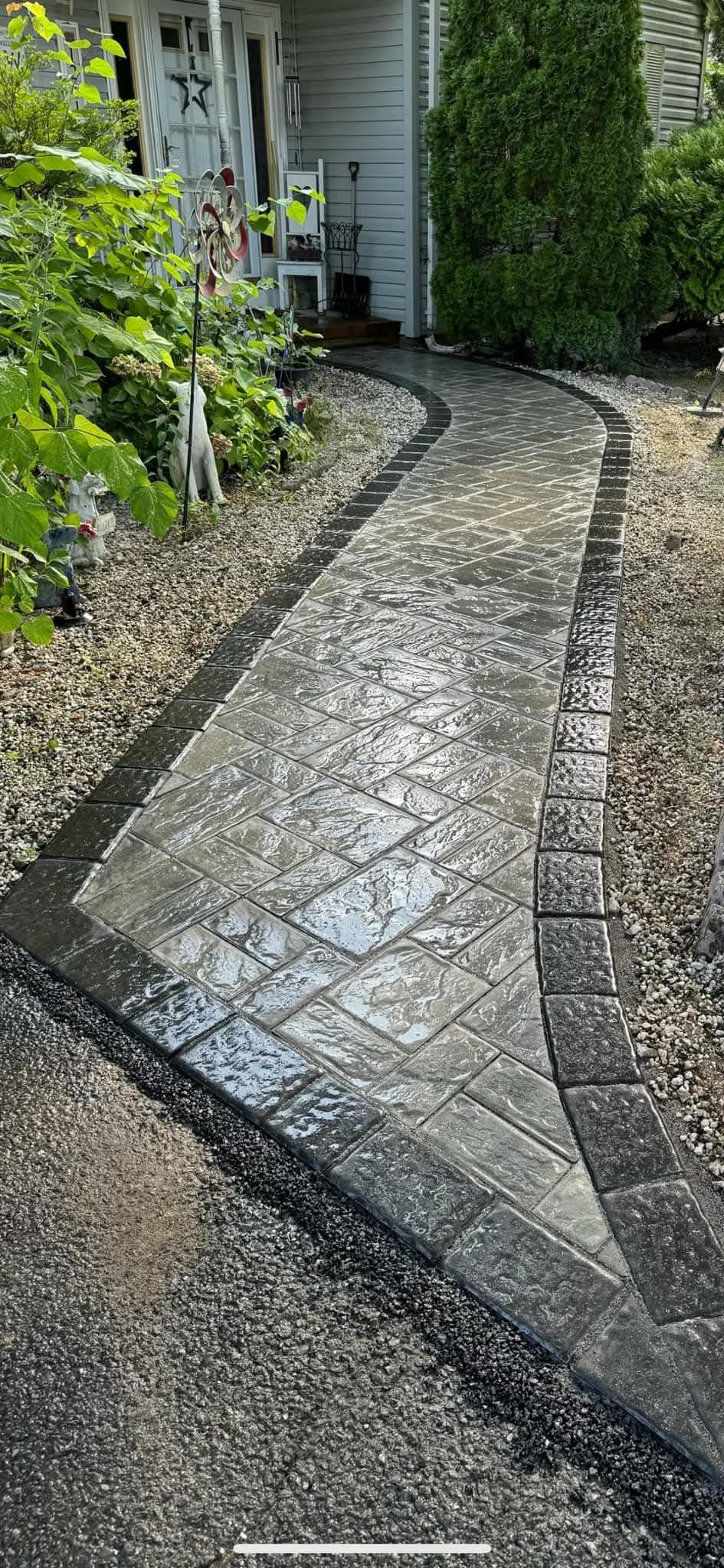 A stone walkway curves through a yard, lined with gravel and greenery.