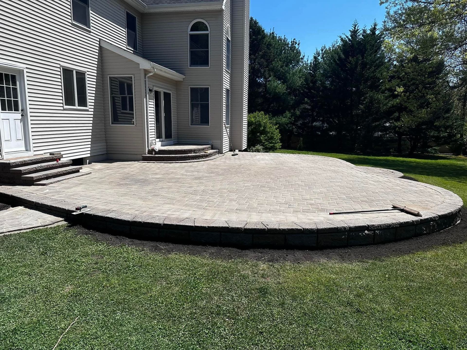 A large outdoor patio next to a beige two-story house; curved retaining wall.