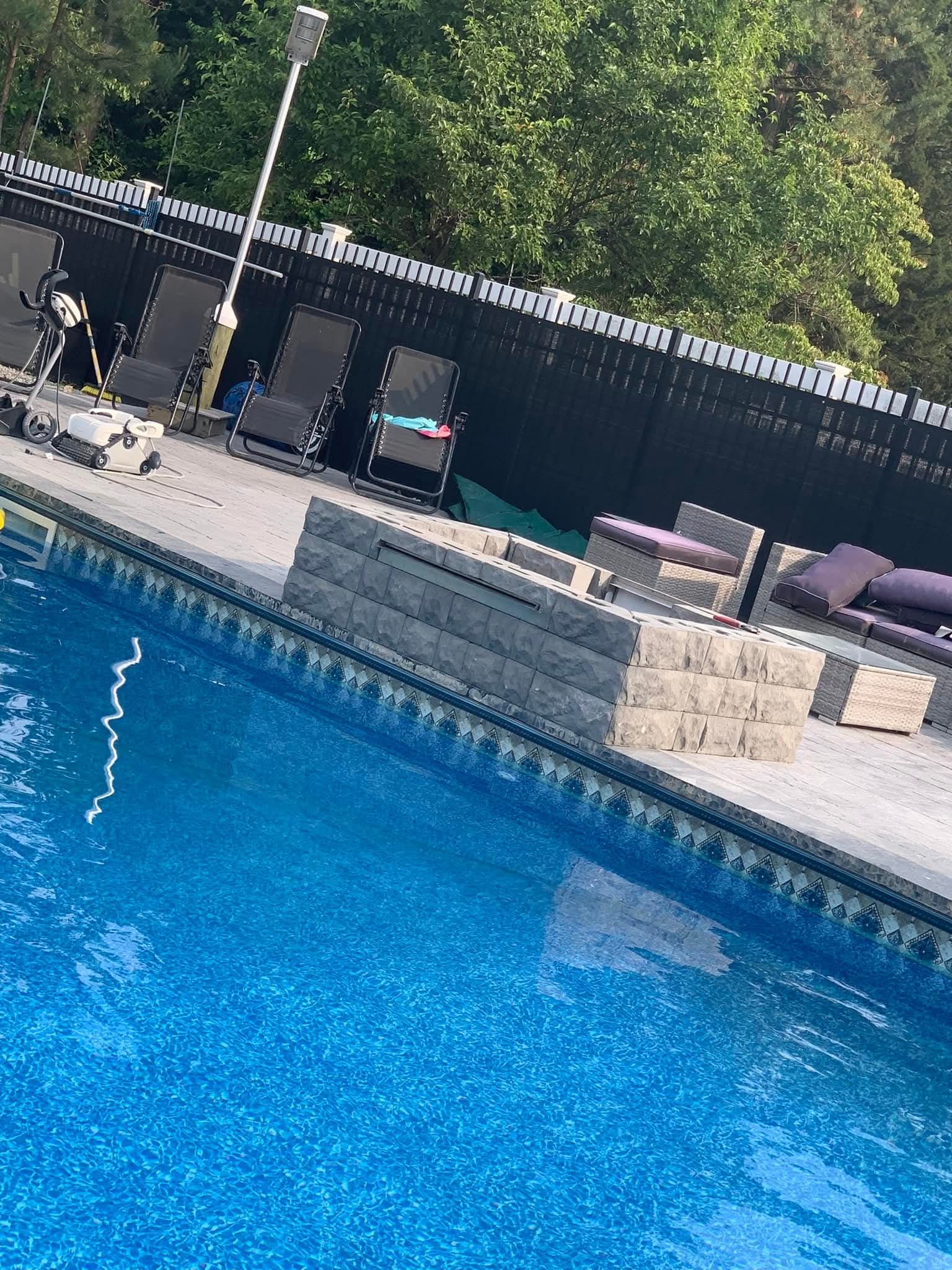 Blue pool with a gray patio, lounge chairs, and a black fence in the background.