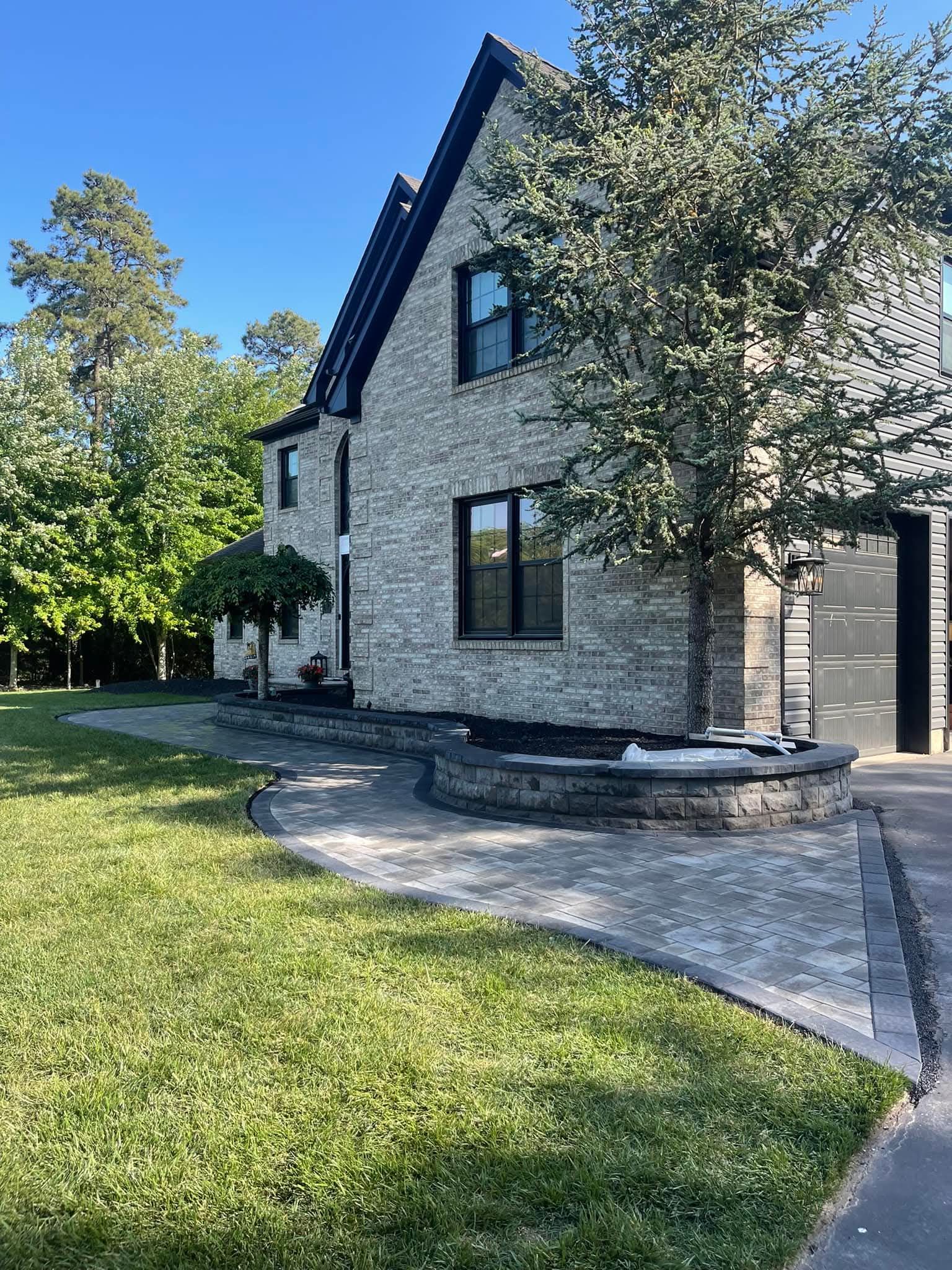 Two-story brick house with a paved walkway, a tree, and green grass.